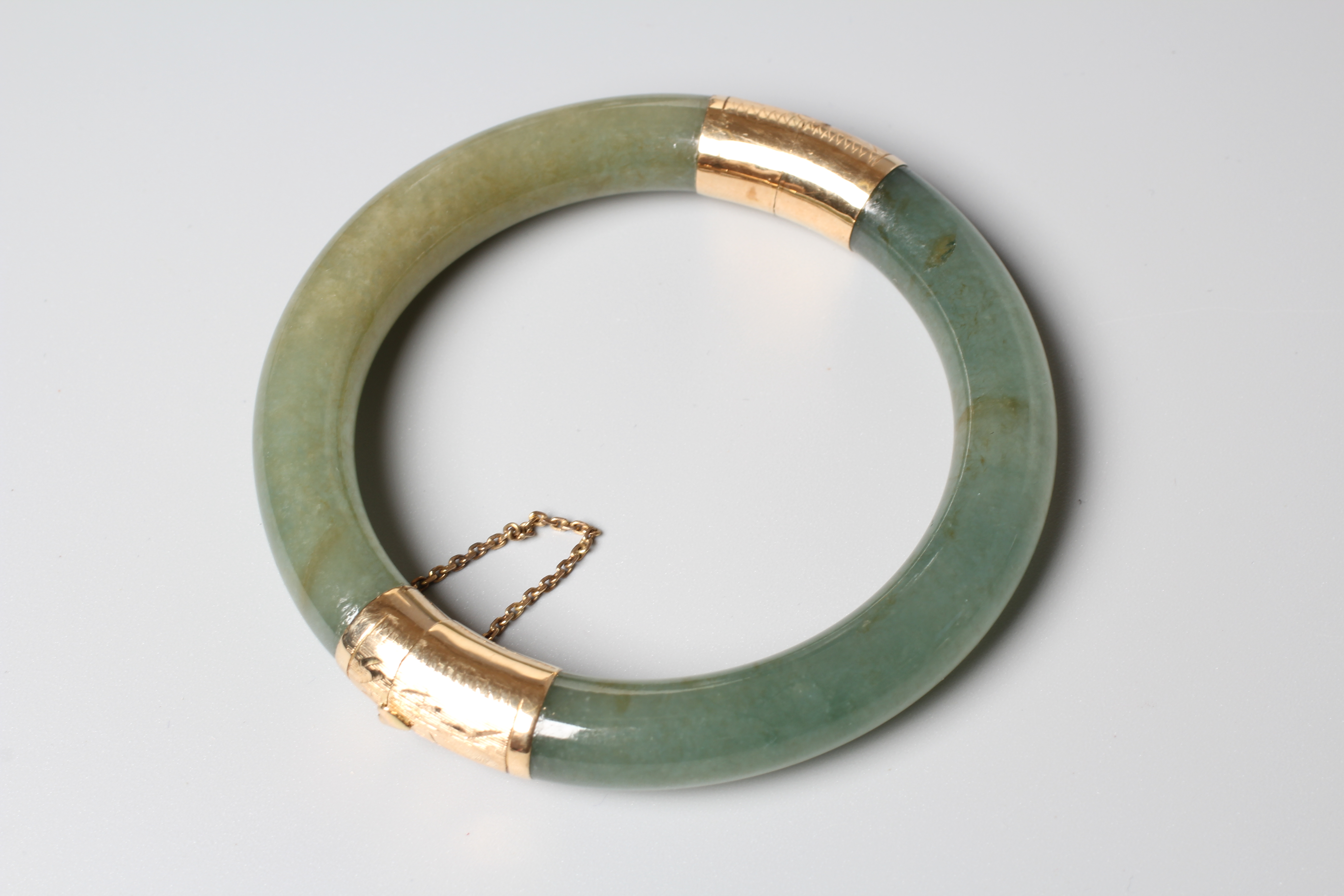 A CHINESE POLISHED JADE STIFF HINGED BANGLE, the two pieces hinged with engraved yellow metal Image