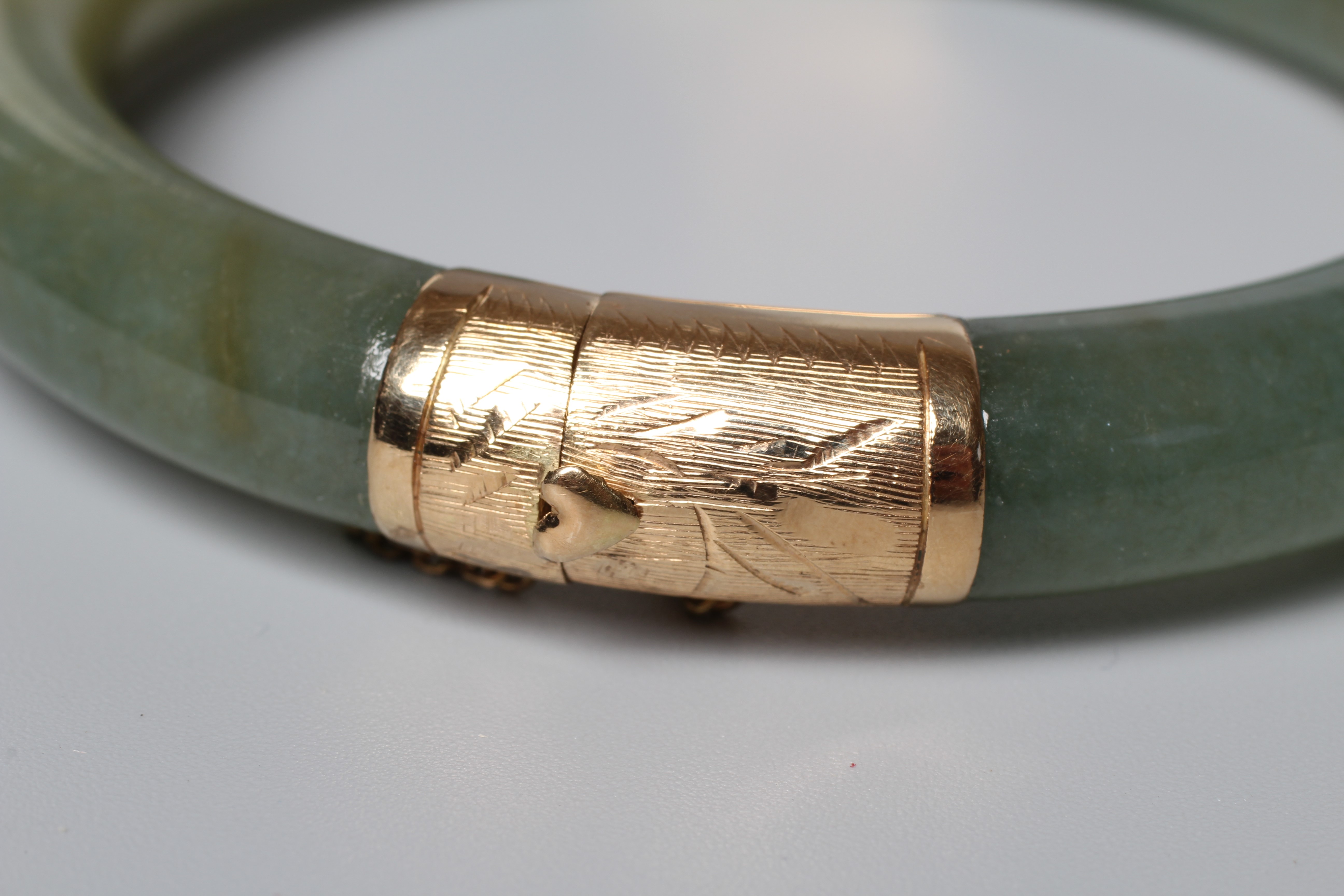 A CHINESE POLISHED JADE STIFF HINGED BANGLE, the two pieces hinged with engraved yellow metal Image