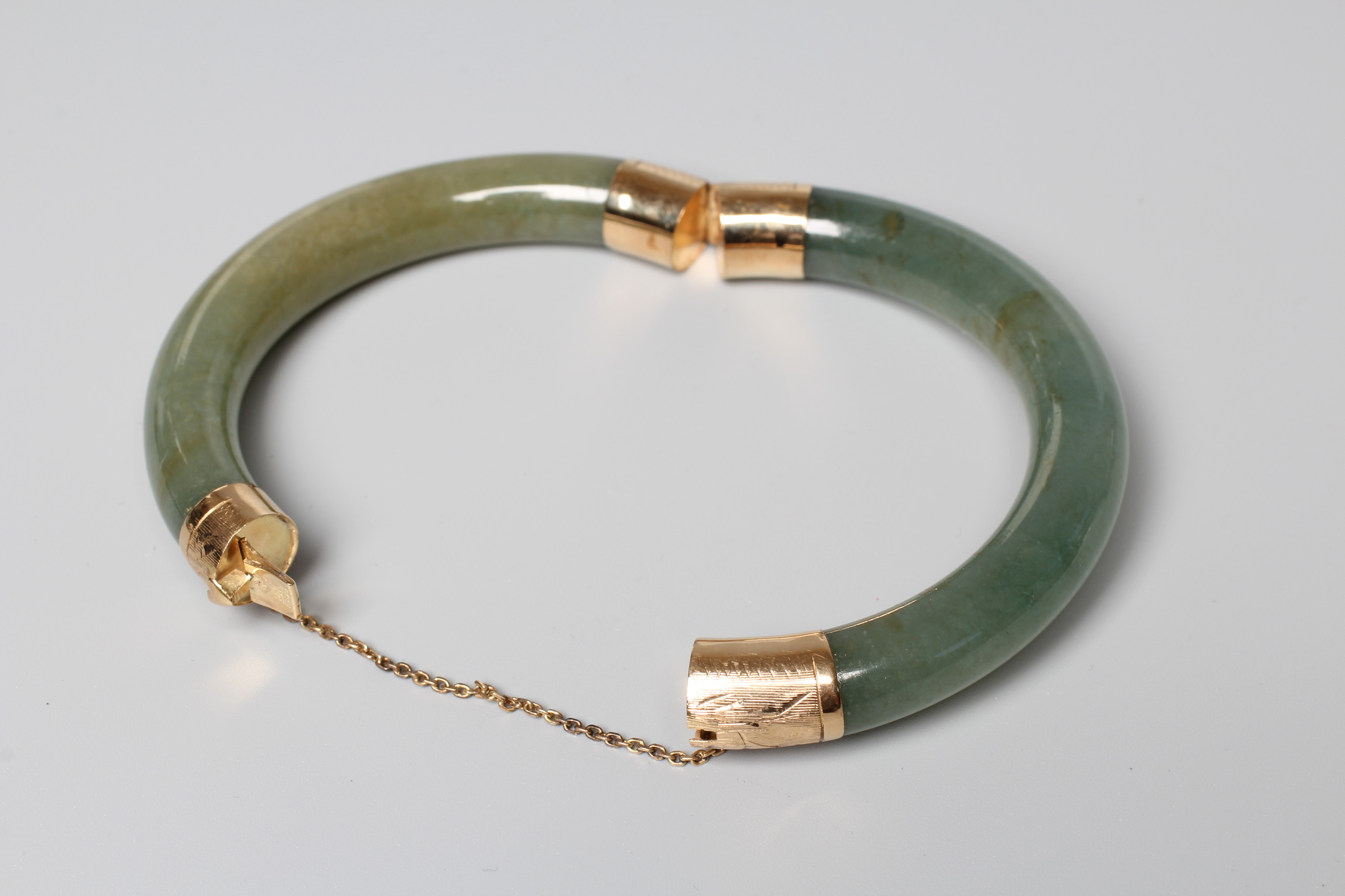 A CHINESE POLISHED JADE STIFF HINGED BANGLE, the two pieces hinged with engraved yellow metal Image