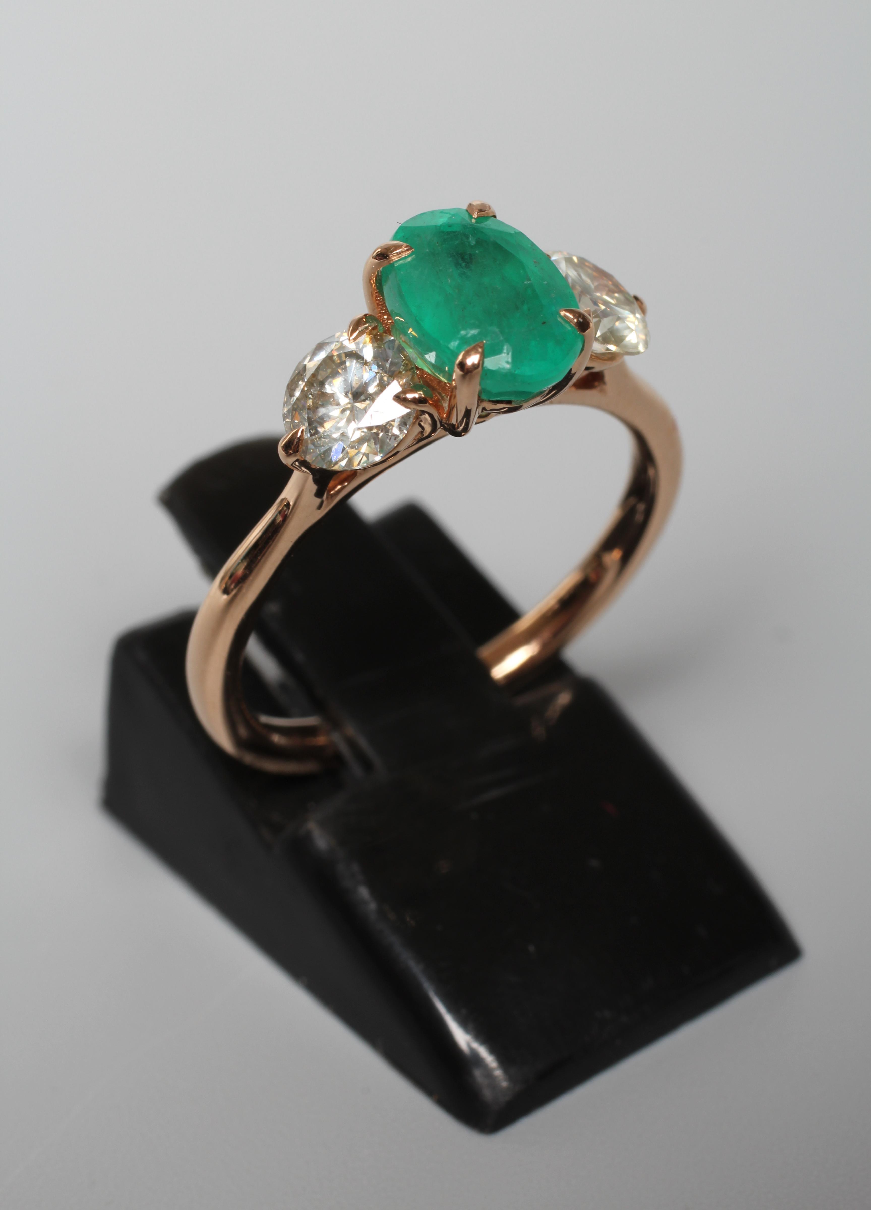 AN EMERALD AND DIAMOND RING, the oval facet cut emerald claw set and flanked by two round brilliant Image
