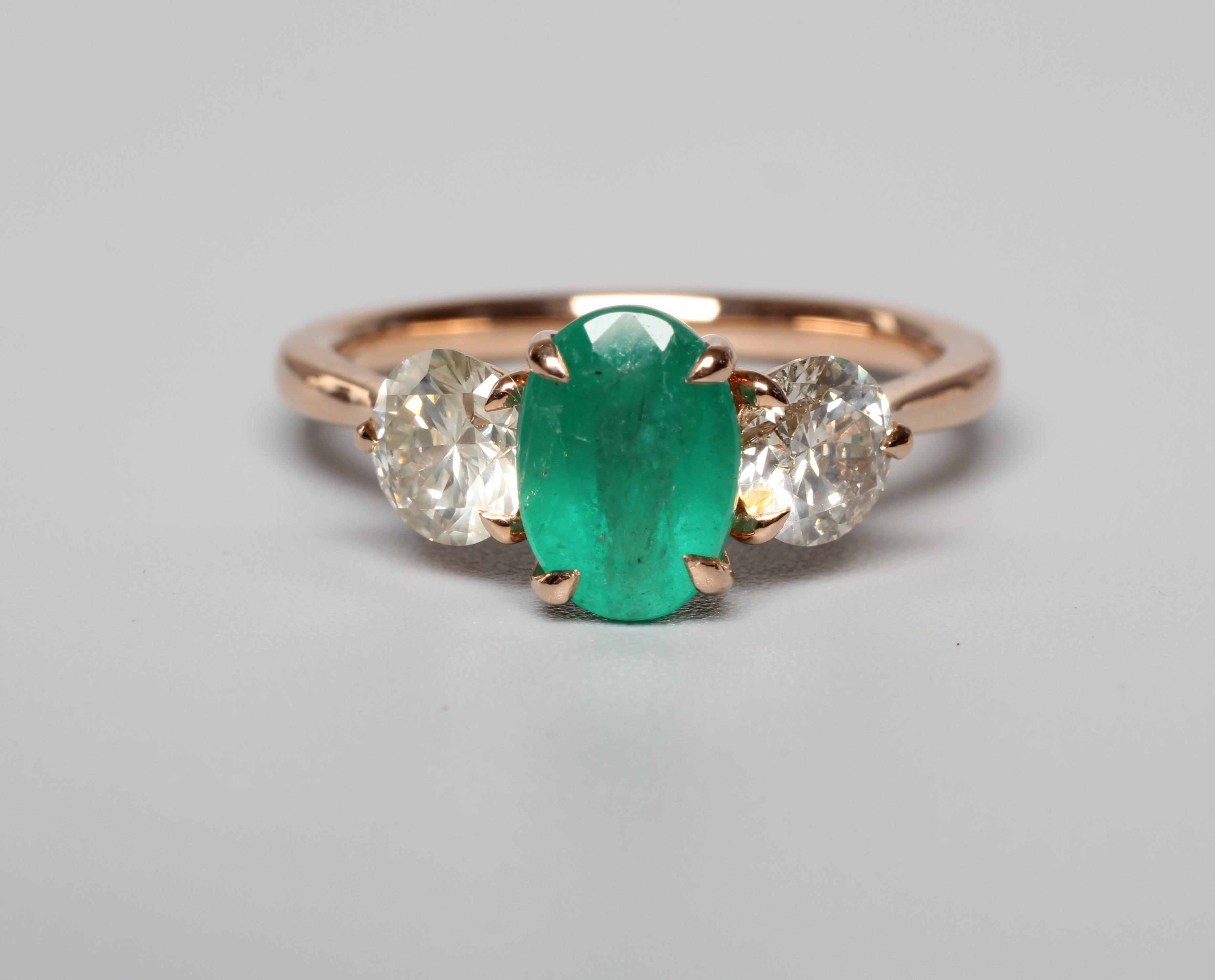 AN EMERALD AND DIAMOND RING, the oval facet cut emerald claw set and flanked by two round brilliant Image