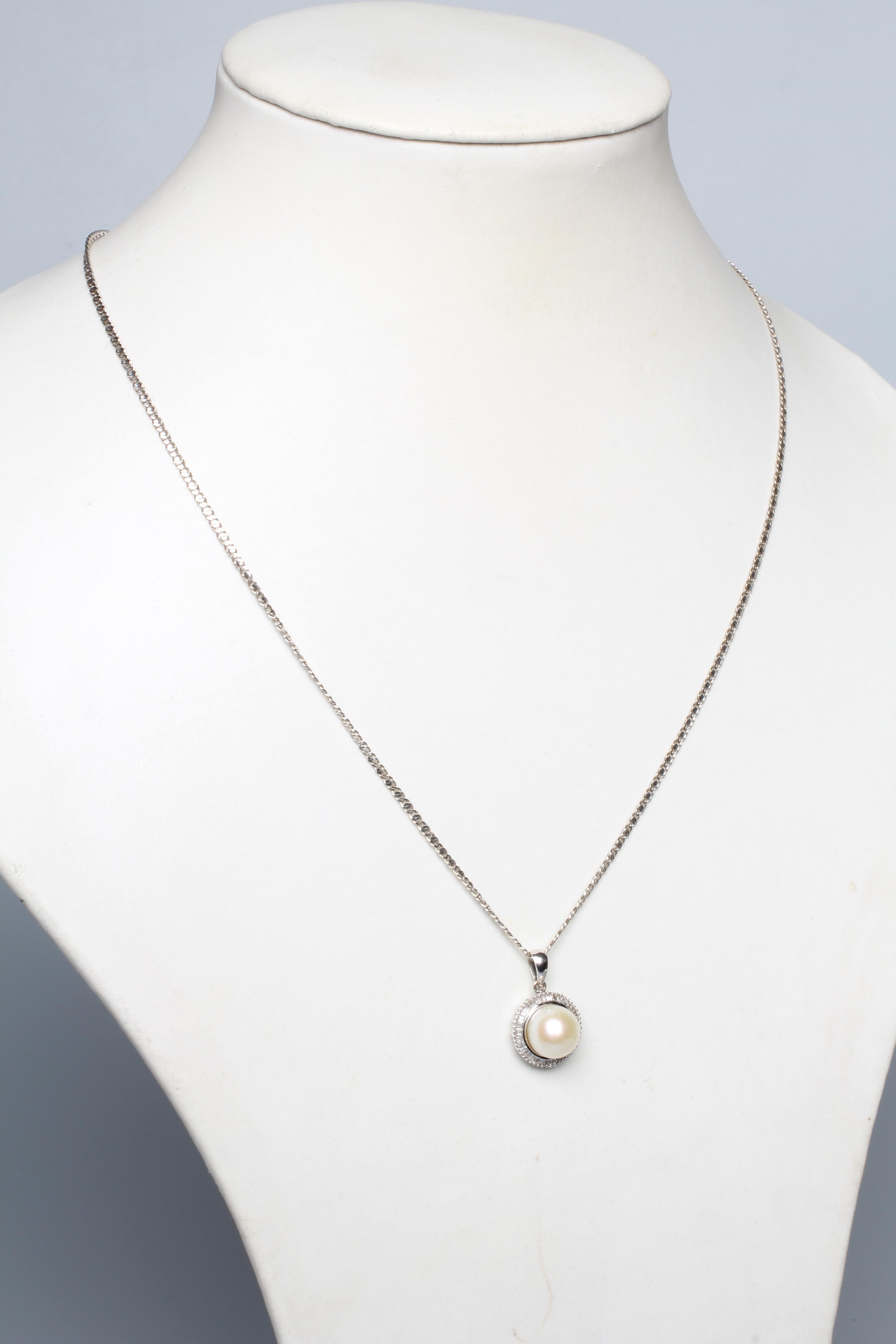 A CULTURED PEARL AND DIAMOND PENDANT, the peg set pearl within a border of small baguette cut Image