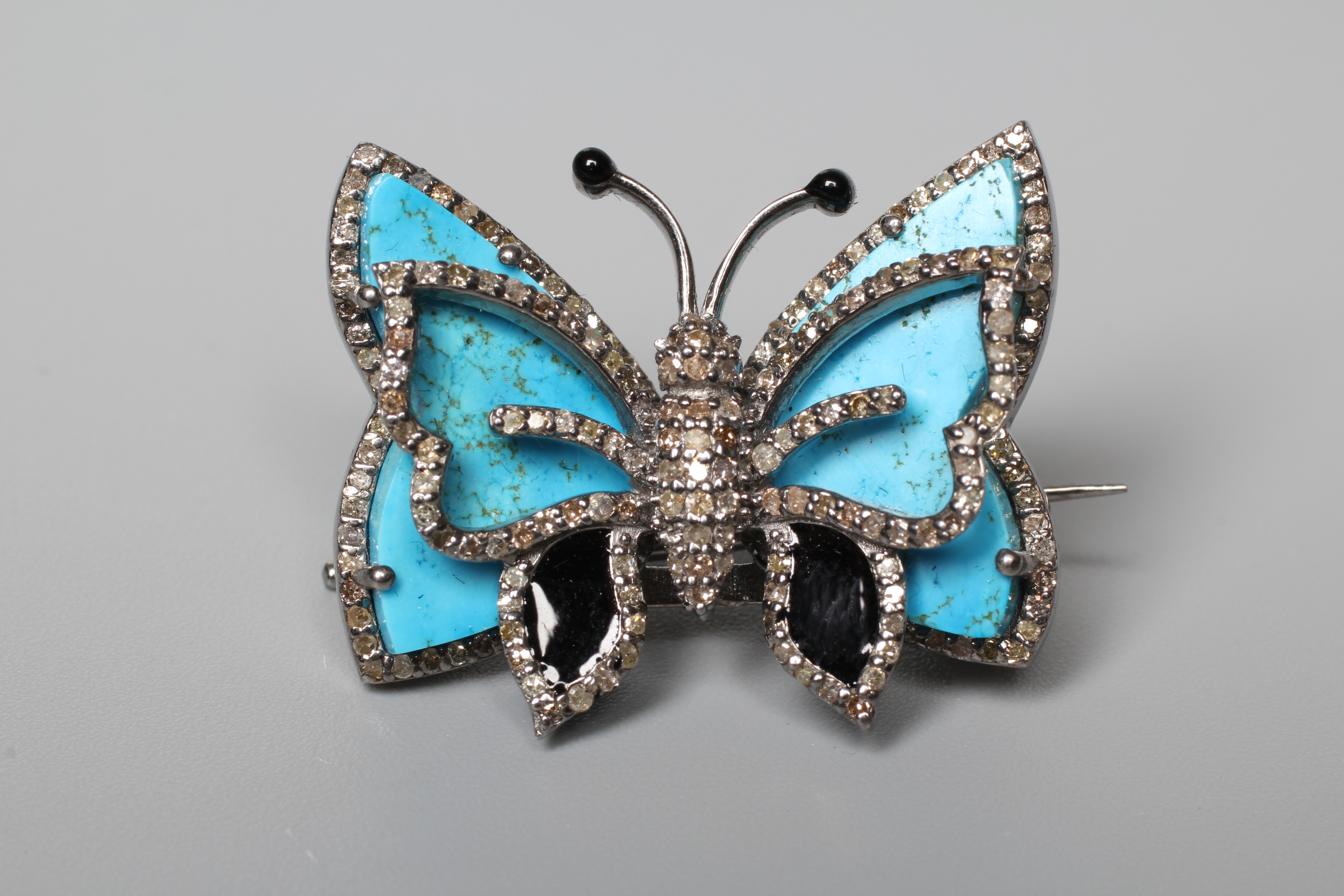 A BUTTERFLY BROOCH, the unmarked silver frame inset with turquoise wings with black enamel tips and Image