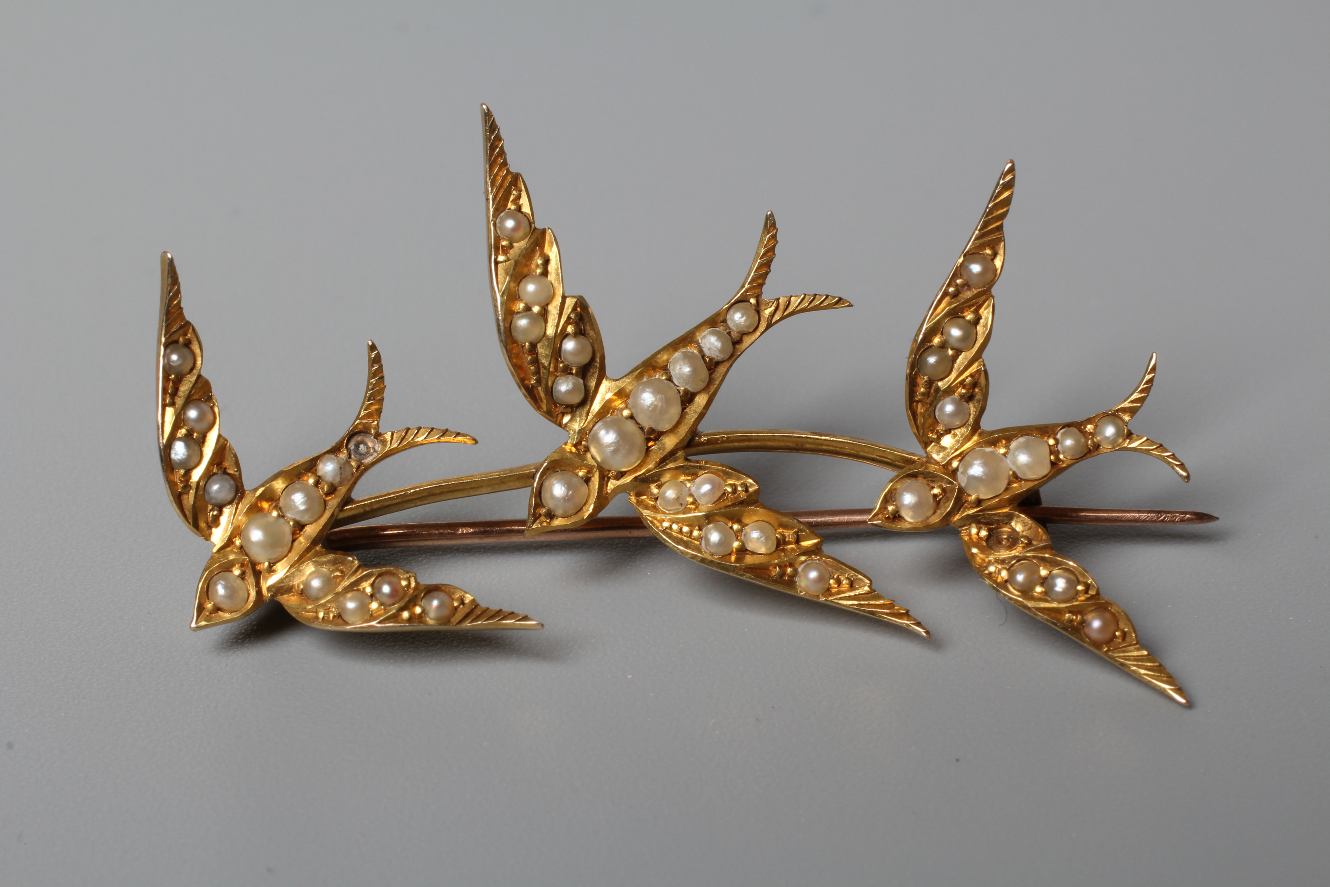 AN EDWARDIAN SEED PEARL TRIPLE SWALLOW BROOCH, the graduating birds set to a plain knife edge bar Image