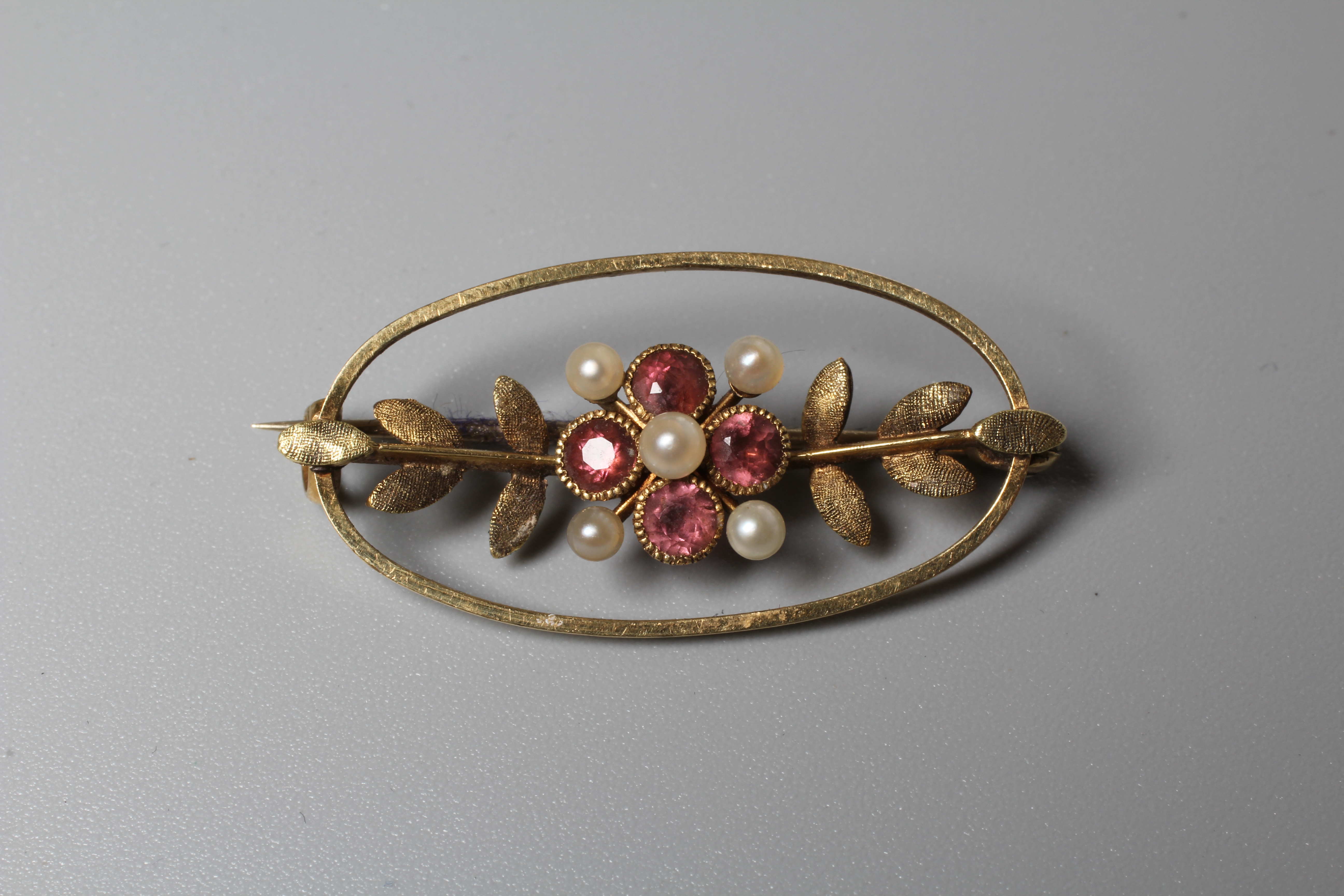 AN EDWARDIAN ALMANDINE GARNET OVAL BROOCH, the open panel centred by a garnet set flowerhead with Image