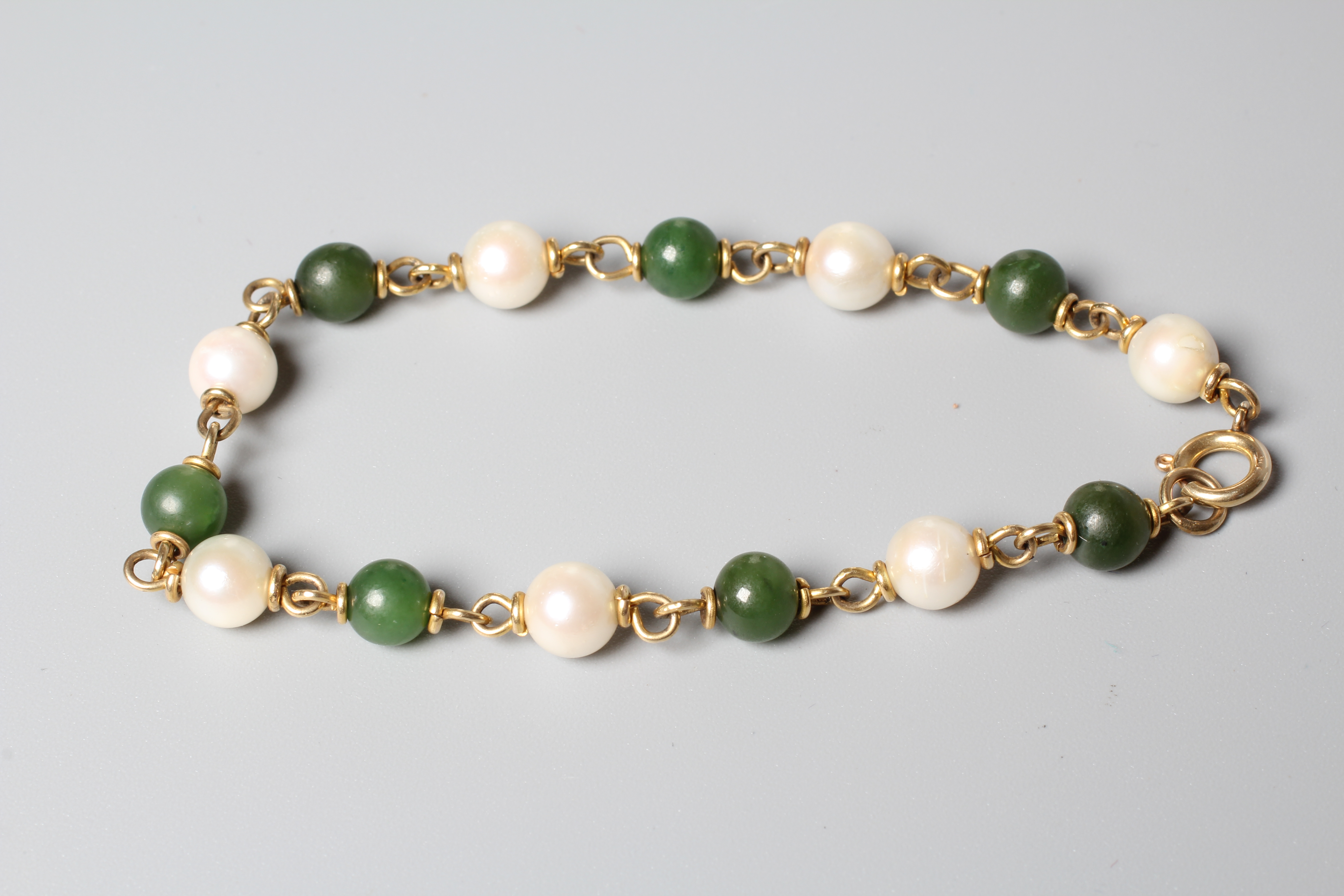 A CULTURED PEARL AND POLISHED JADE BEAD BRACELET, the seven pearls and beads peg set to plain metal Image