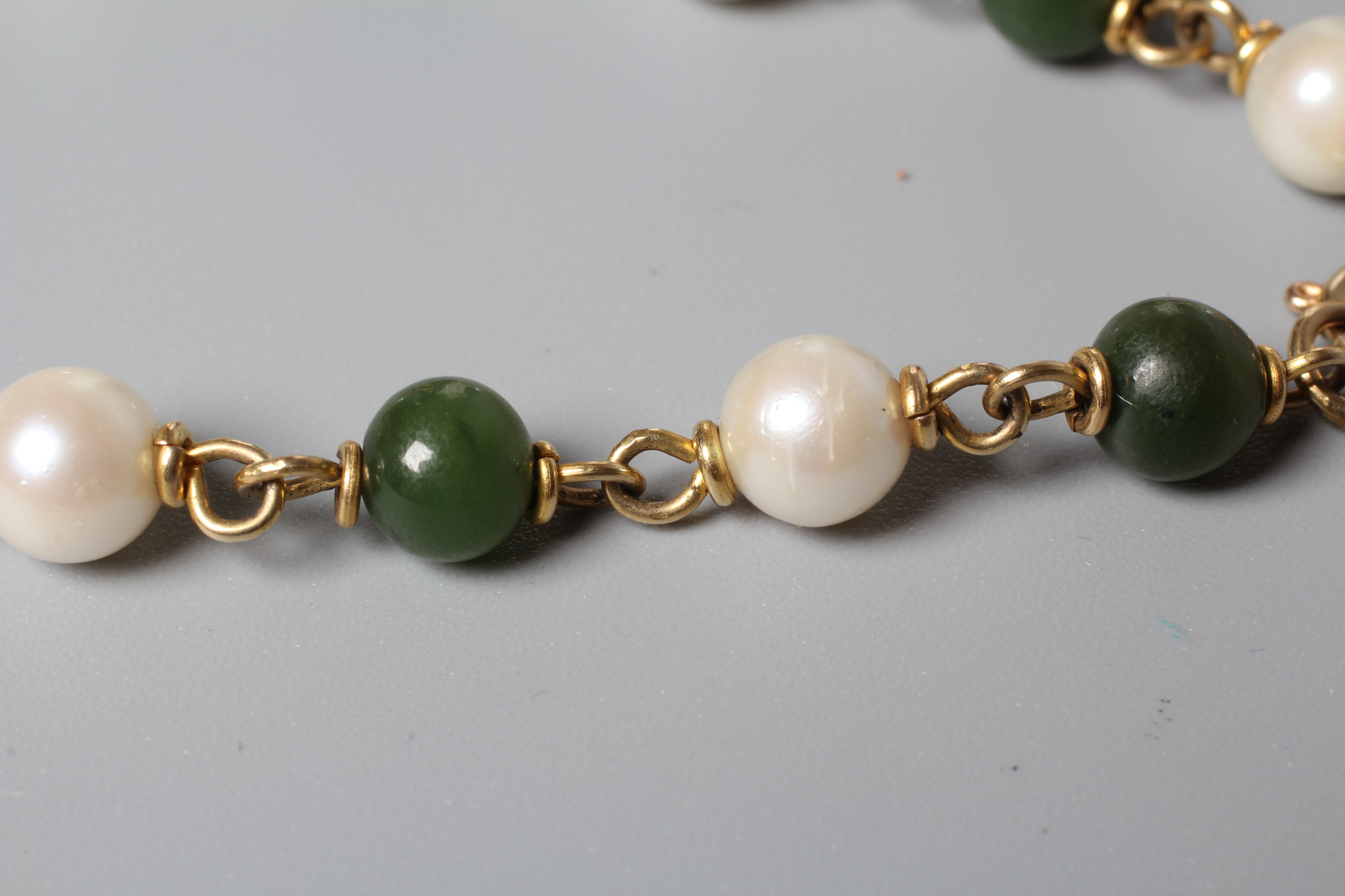 A CULTURED PEARL AND POLISHED JADE BEAD BRACELET, the seven pearls and beads peg set to plain metal Image