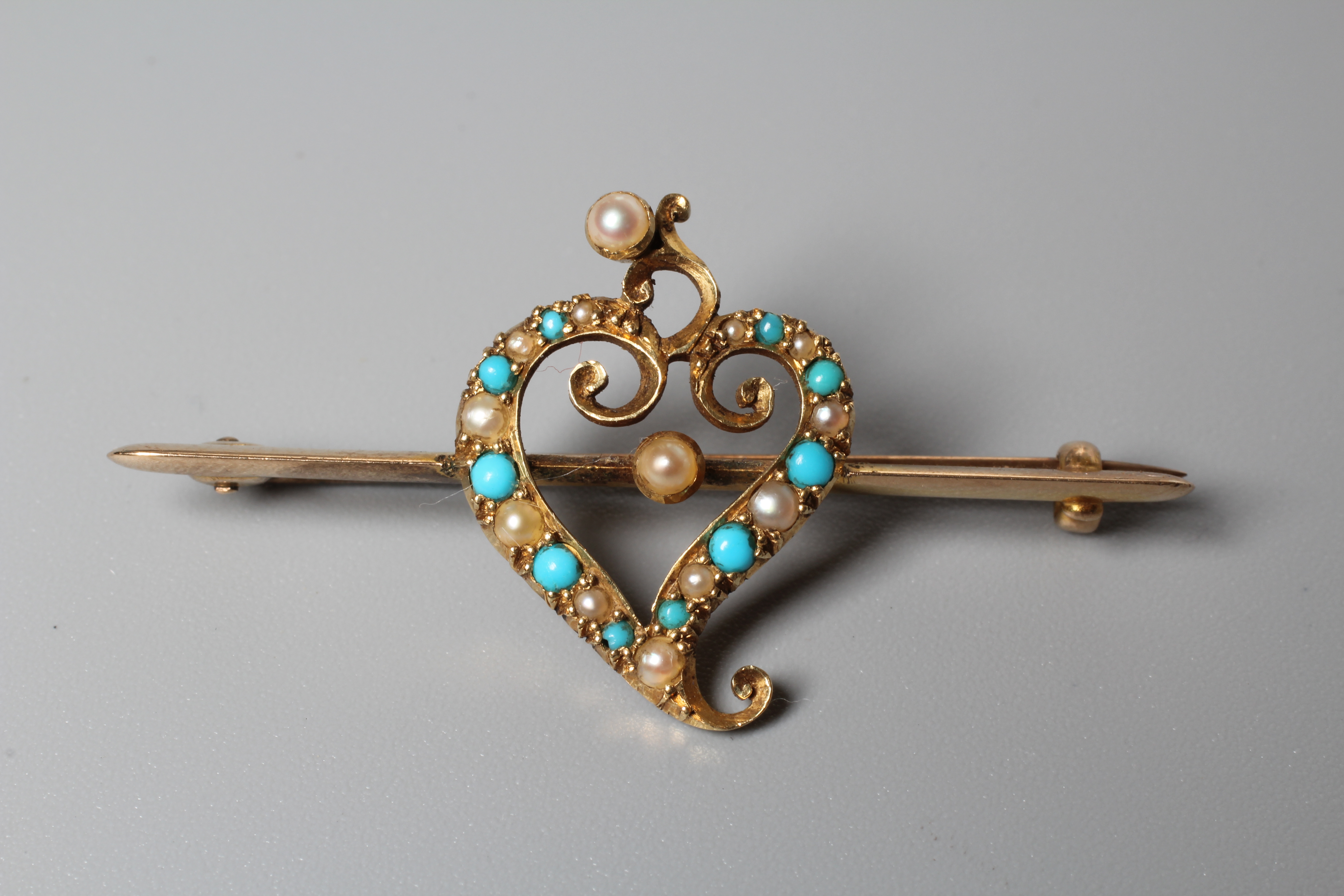 AN EDWARDIAN SEED PEARL AND TURQUOISE BAR BROOCH, the central open heart on an unmarked knife edge Image