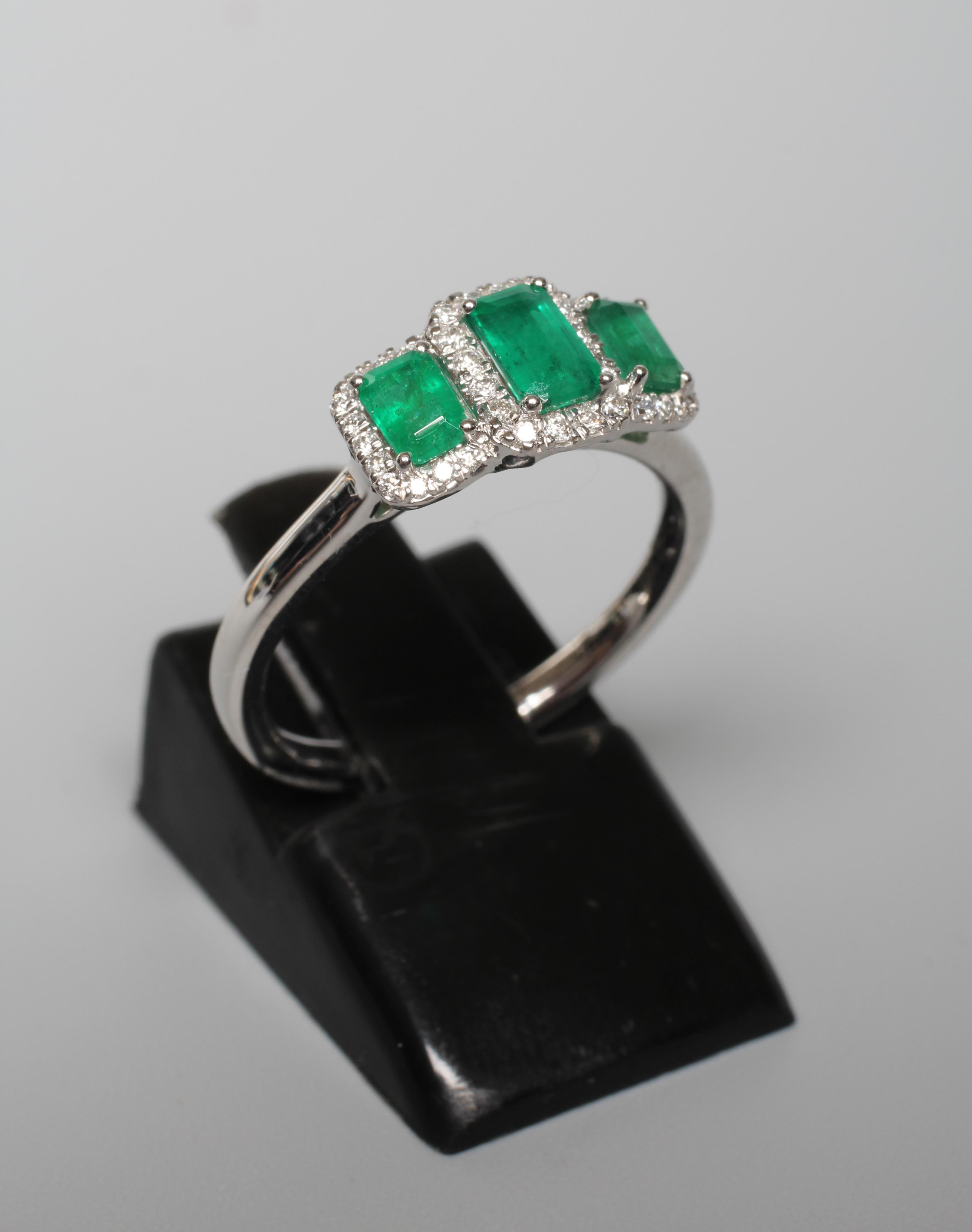 A THREE STONE EMERALD RING, the step cut stones claw set to borders of small round brilliant cut Image