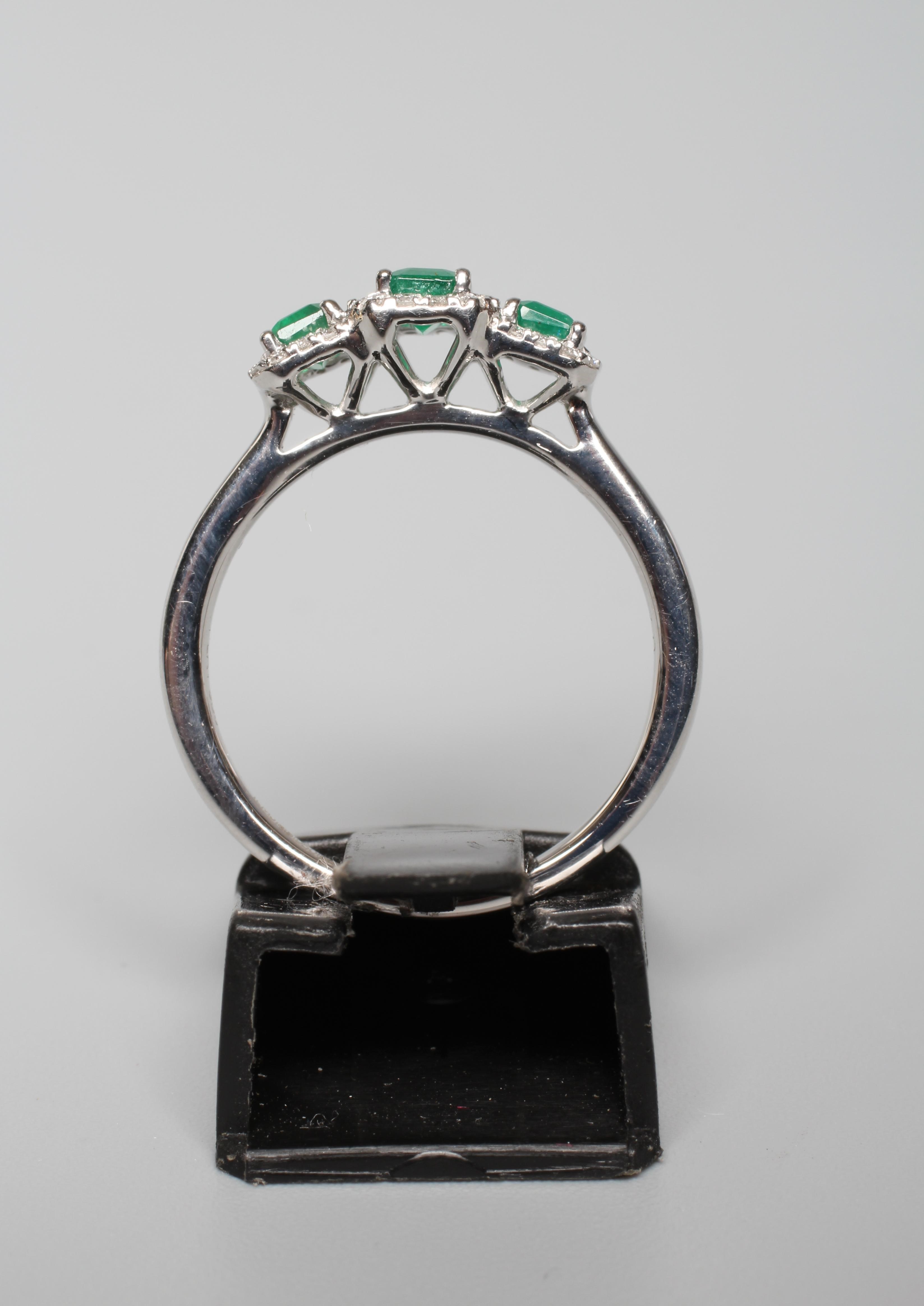 A THREE STONE EMERALD RING, the step cut stones claw set to borders of small round brilliant cut Image