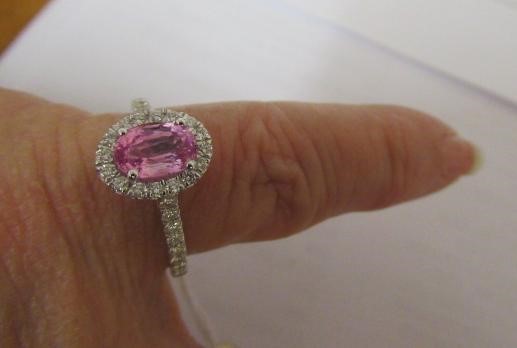 A PINK SAPPHIRE AND DIAMOND CLUSTER RING, the oval facet cut sapphire claw set to a border of small Image