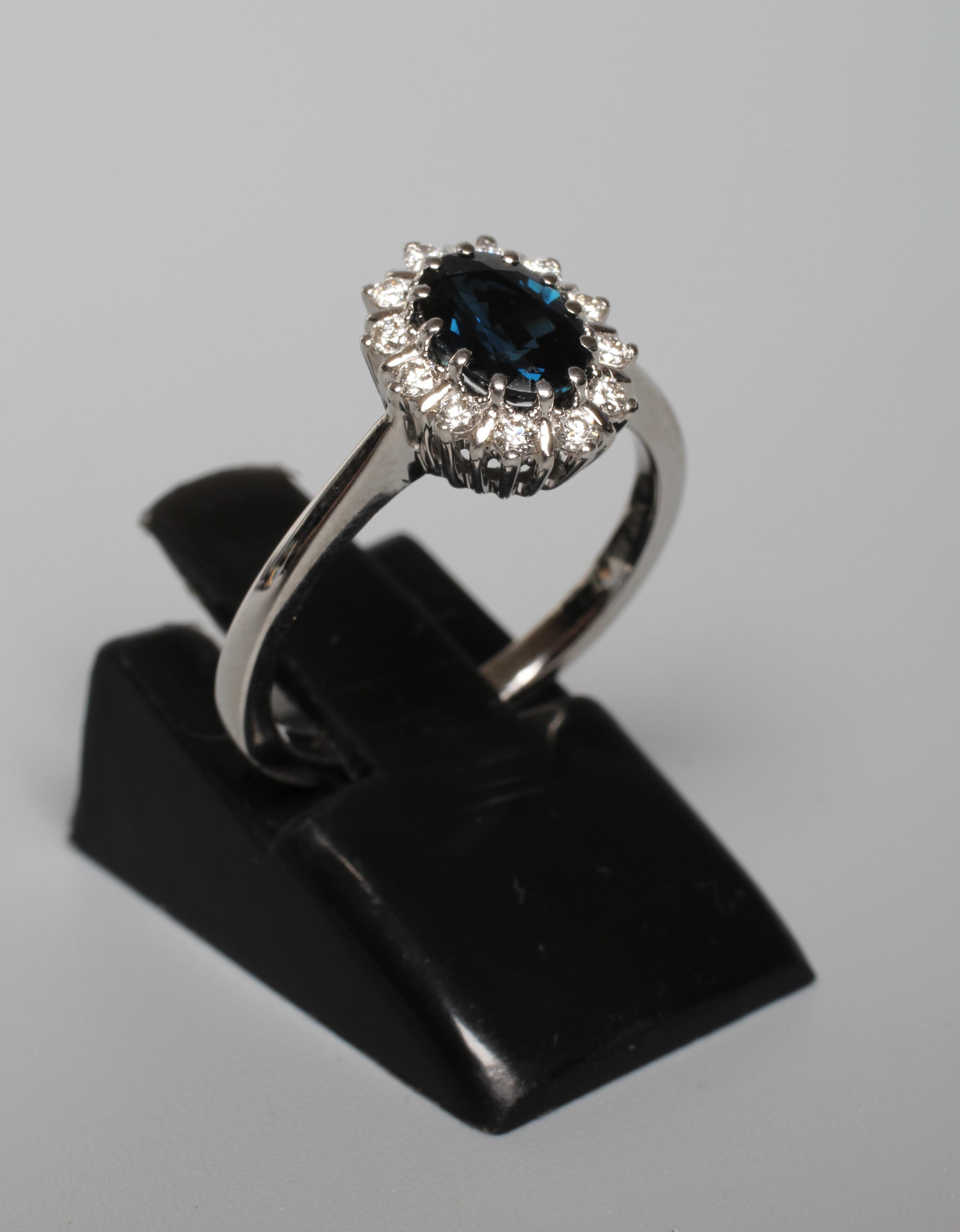 A SAPPHIRE AND DIAMOND CLUSTER RING, the oval facet cut sapphire claw set to a border of twelve Image