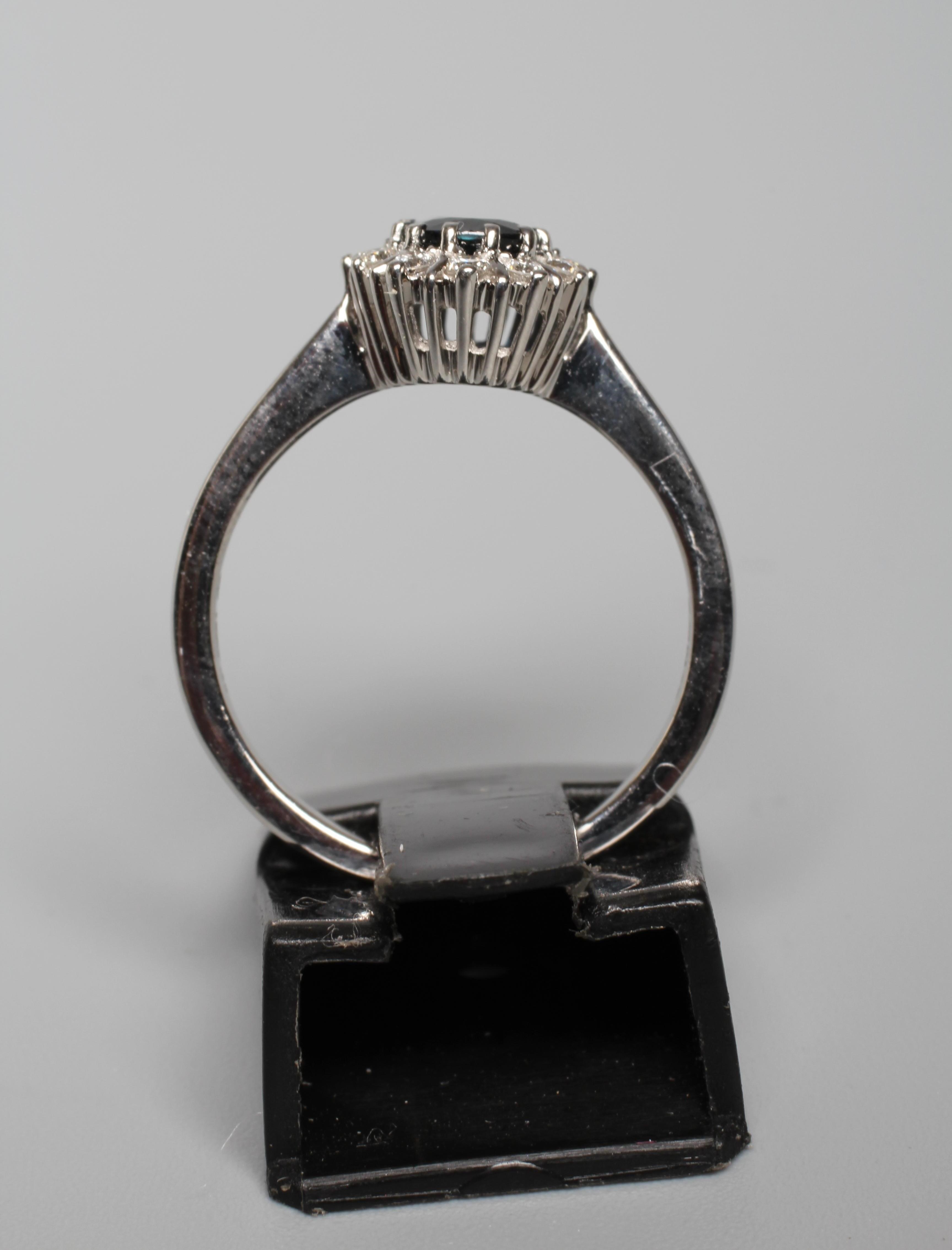 A SAPPHIRE AND DIAMOND CLUSTER RING, the oval facet cut sapphire claw set to a border of twelve Image