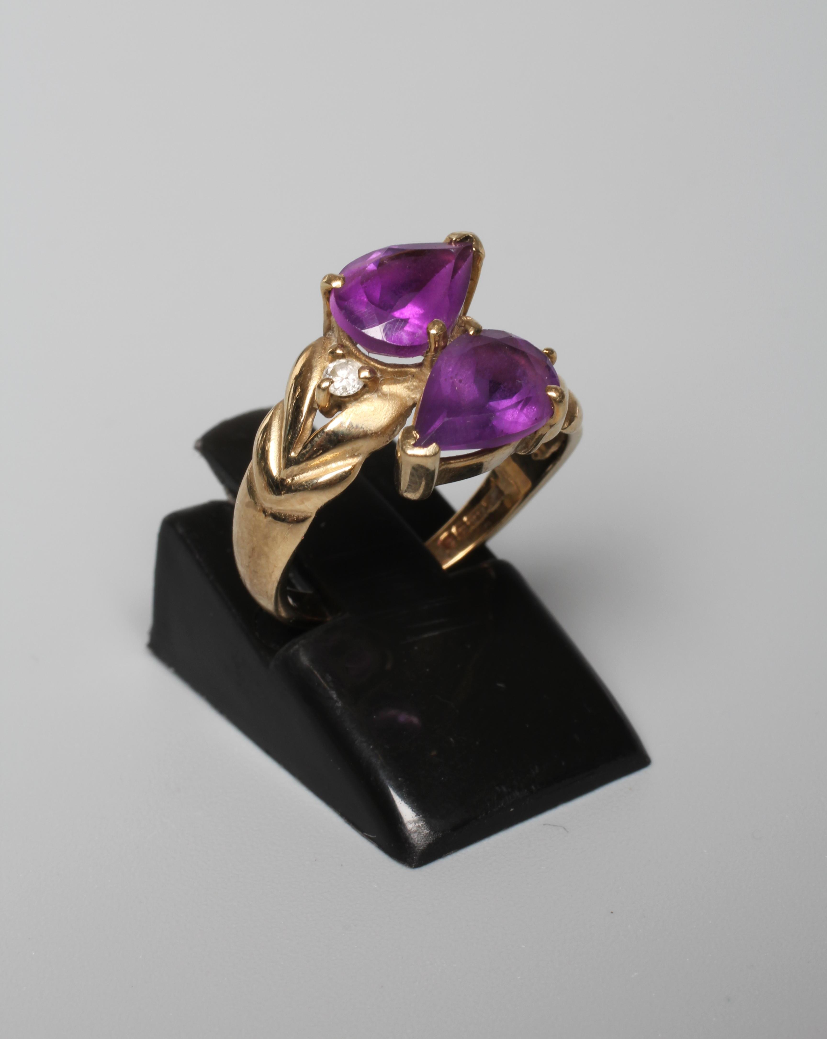 AN AMETHYST DRESS RING, the two pear cut stones vertically claw set with a small round brilliant cut Image