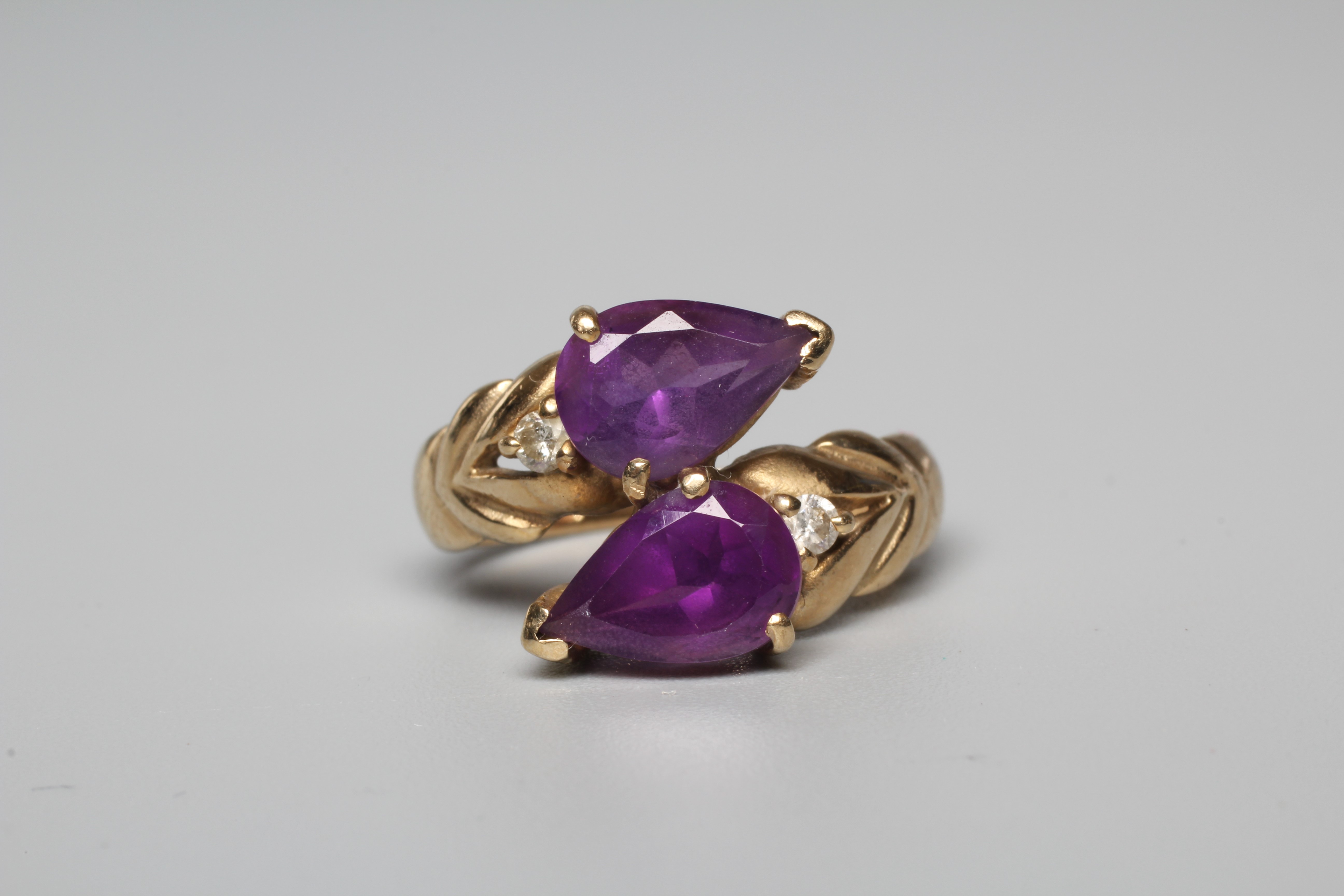 AN AMETHYST DRESS RING, the two pear cut stones vertically claw set with a small round brilliant cut Image