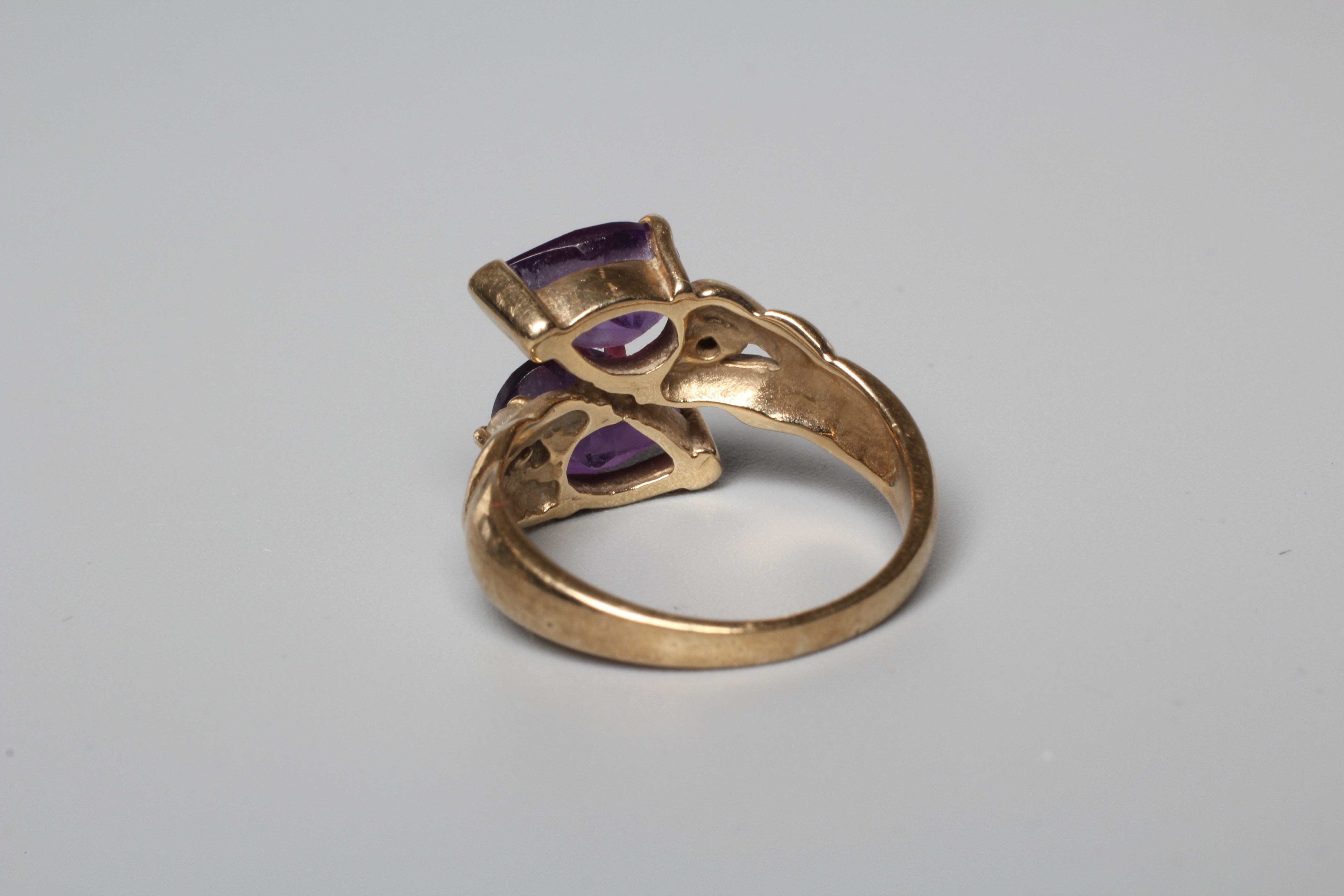 AN AMETHYST DRESS RING, the two pear cut stones vertically claw set with a small round brilliant cut Image