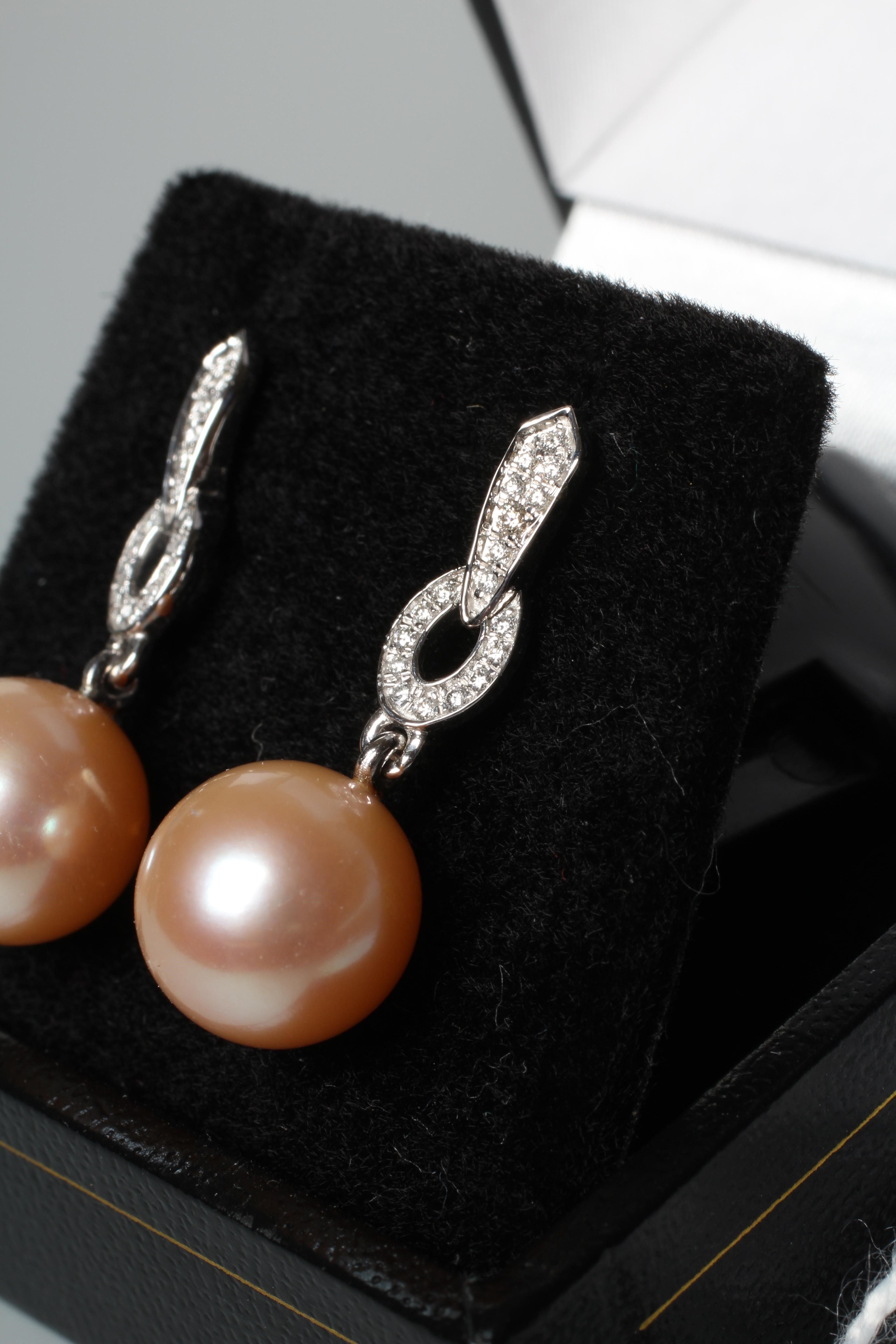 A PAIR OF CULTURED PEARL EAR DROPS, the peach coloured pearls peg set and pendant from an Art Deco Image
