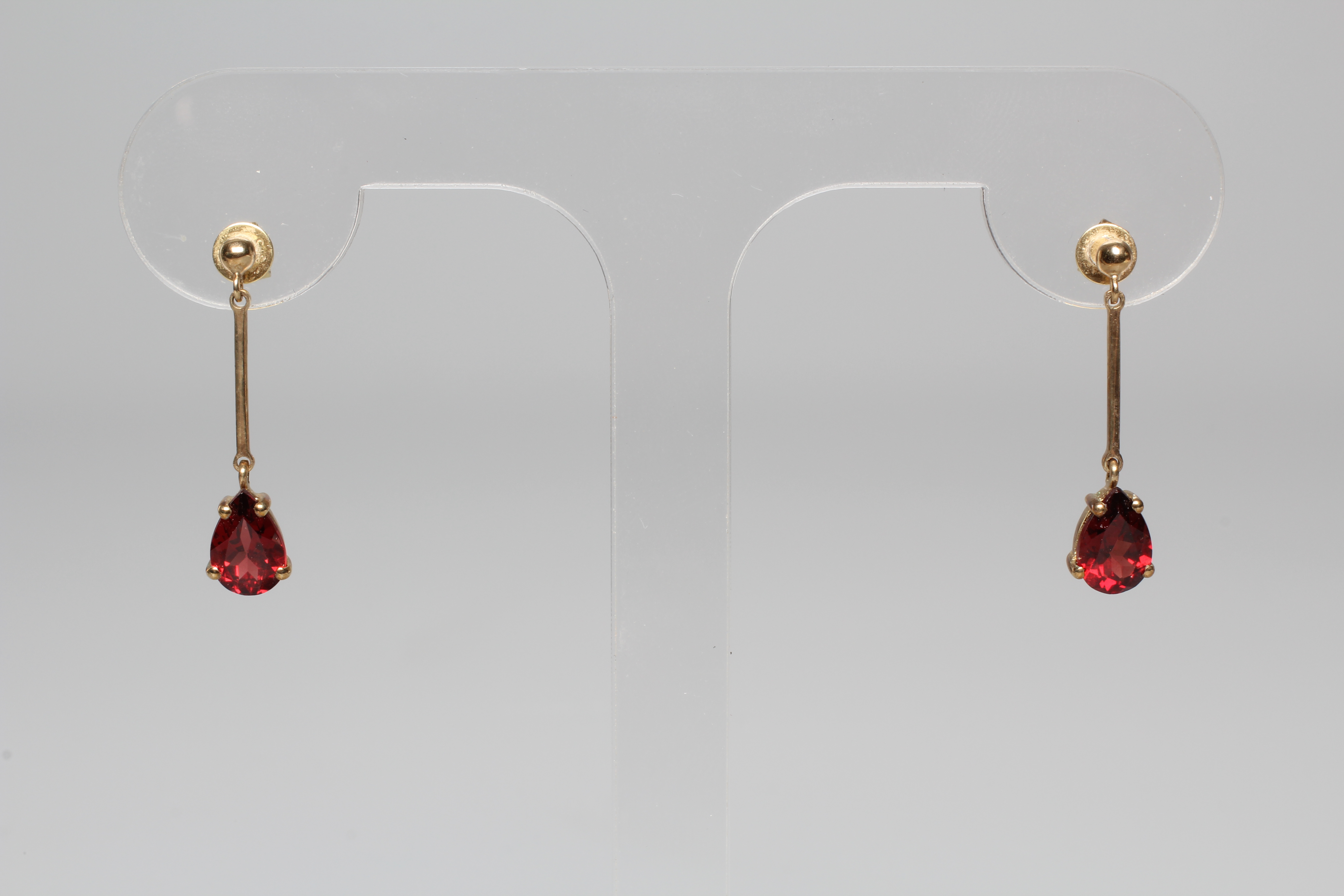 A PAIR OF GARNET DROP EAR STUDS, the pear cut stones pendant from knife edge bars and a plain stud Image