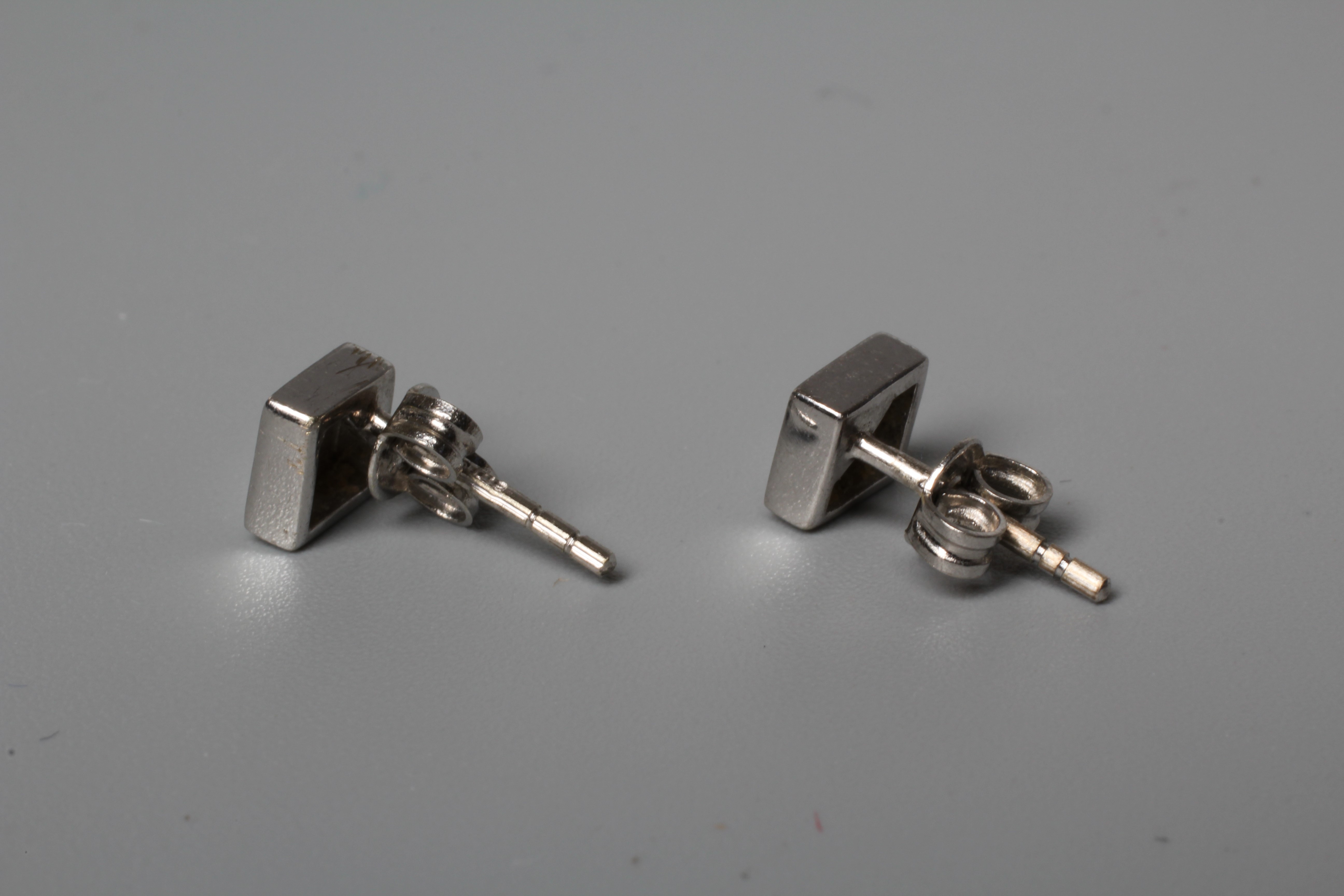 A PAIR OF DIAMOND EAR STUDS, the plain white square panels each set with a small round brilliant to Image