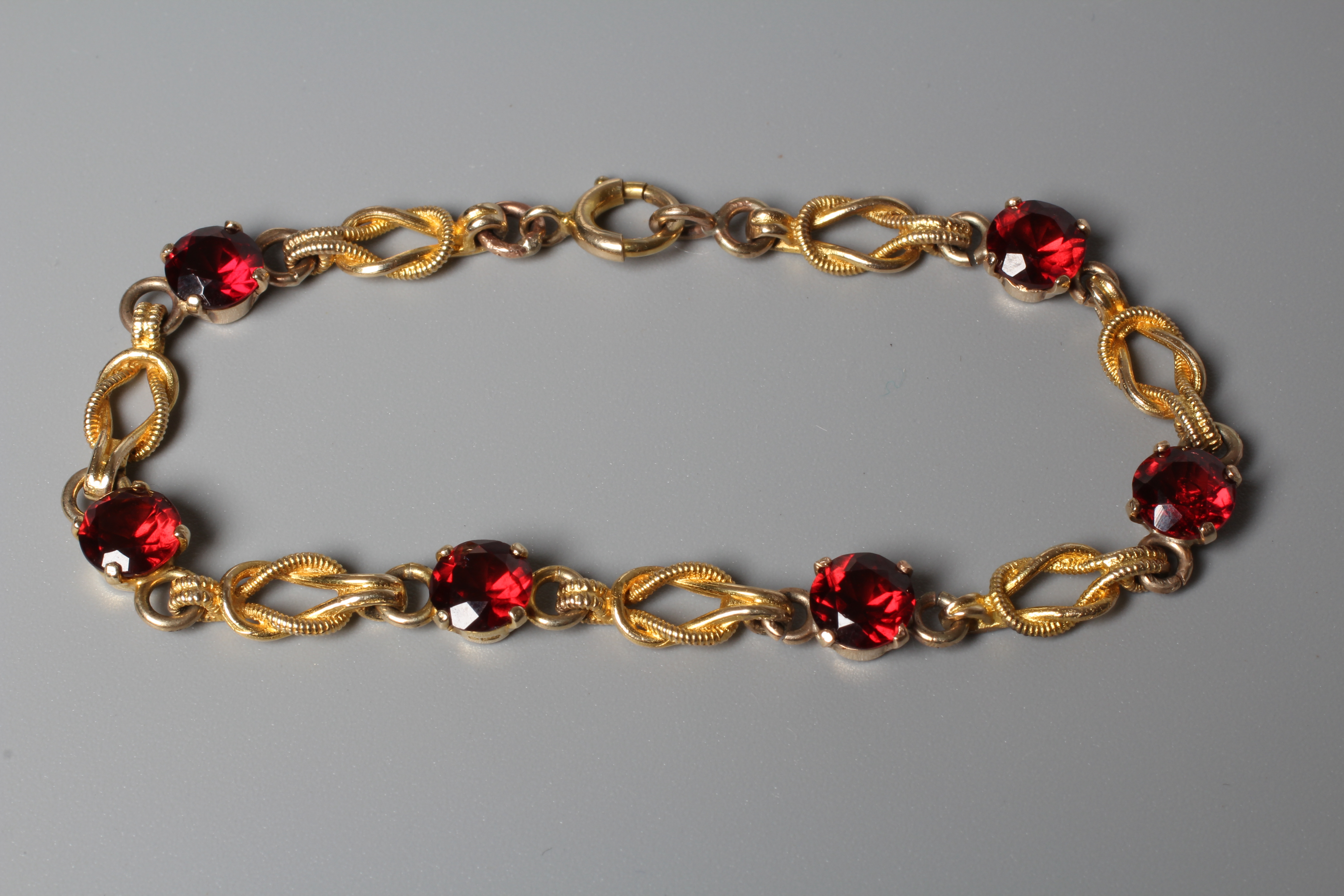 A GARNET BRACELET, the six facet cut circular stones claw set to knot links, the spring ring clasp Image