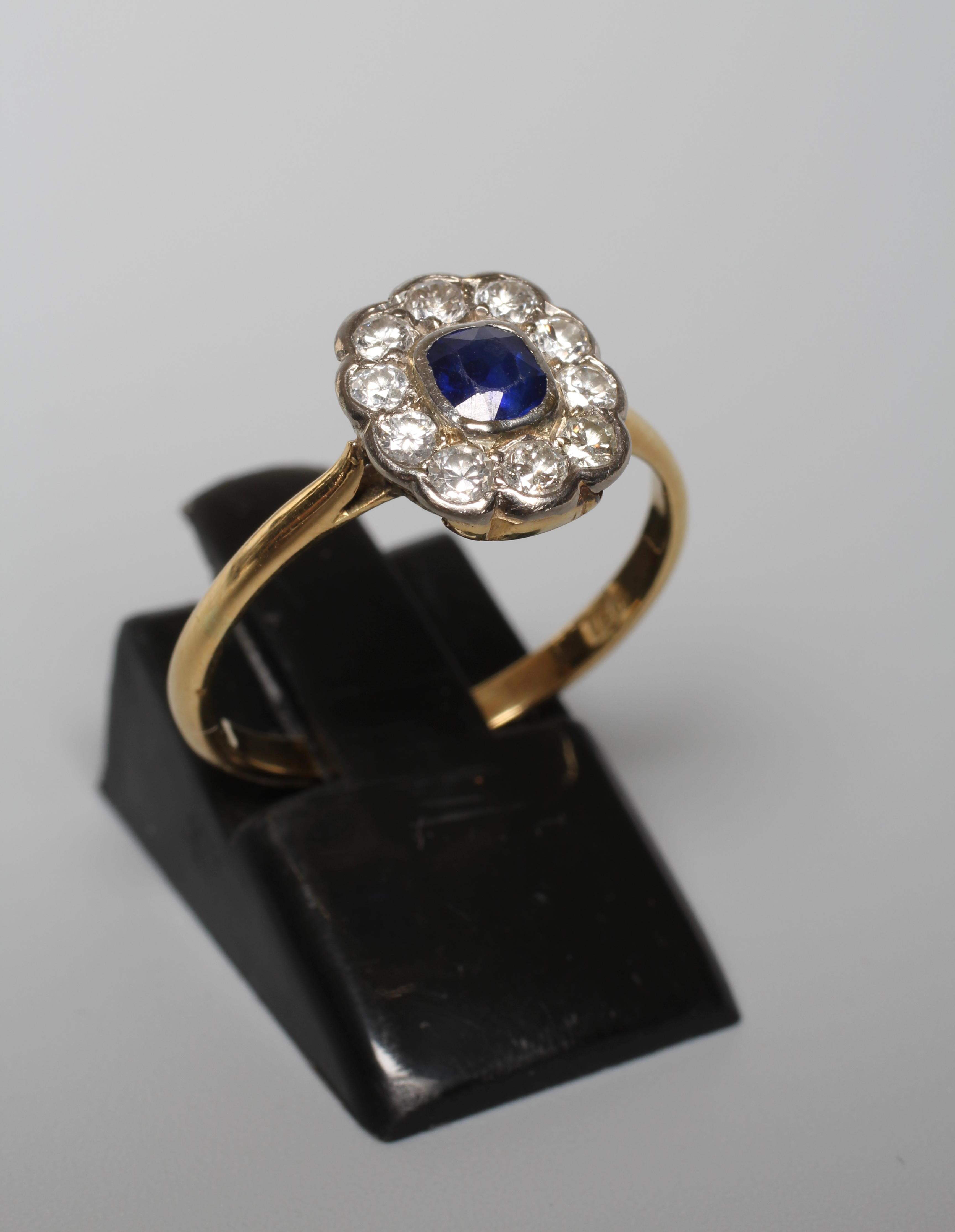 A SAPPHIRE AND DIAMOND CLUSTER RING, the cushion cut sapphire in rub over setting to a border of ten Image