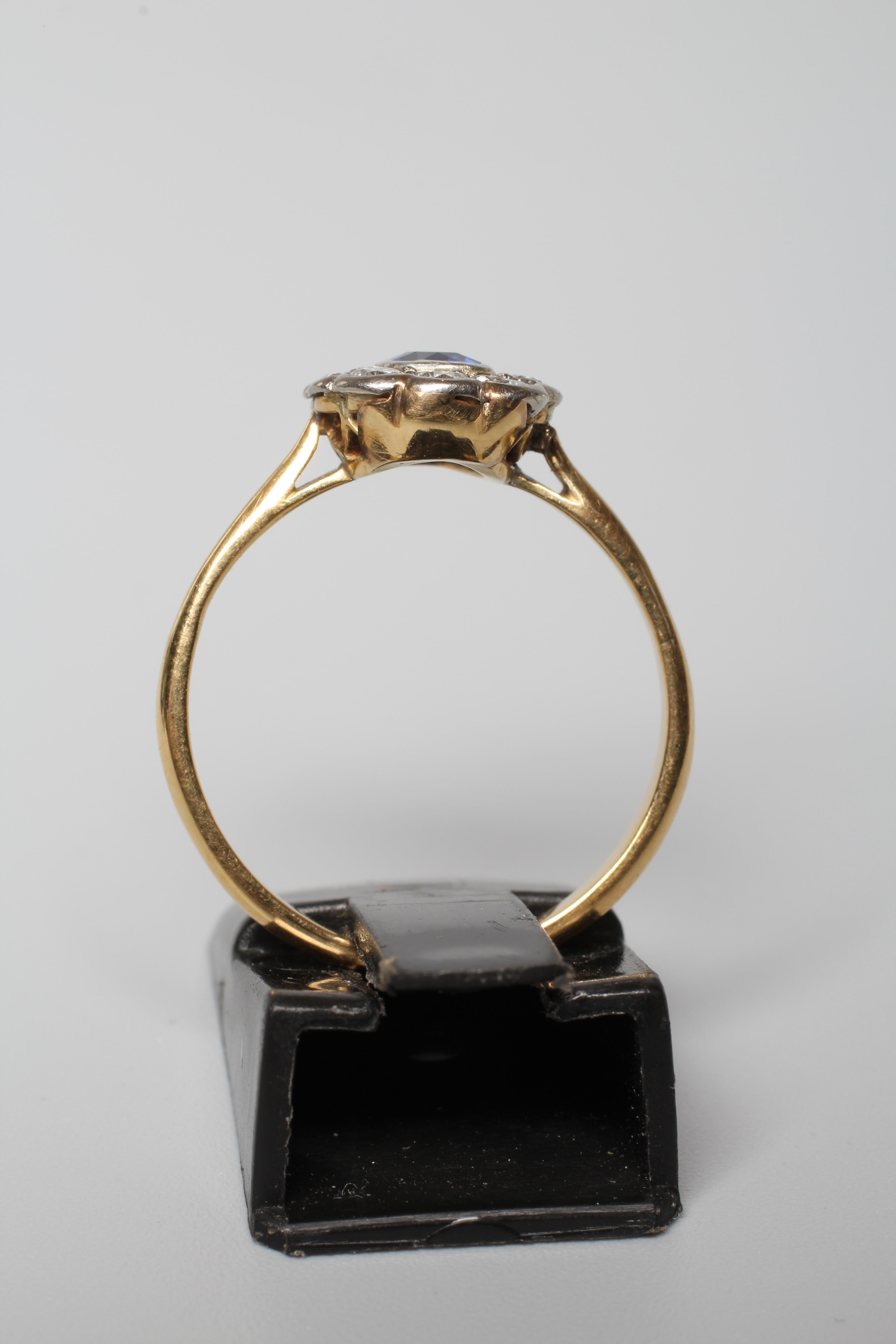 A SAPPHIRE AND DIAMOND CLUSTER RING, the cushion cut sapphire in rub over setting to a border of ten Image
