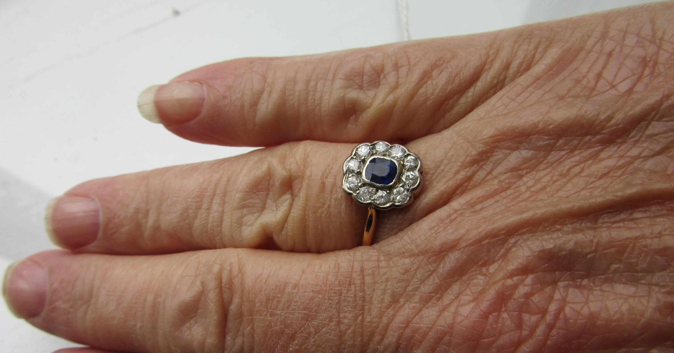 A SAPPHIRE AND DIAMOND CLUSTER RING, the cushion cut sapphire in rub over setting to a border of ten Image