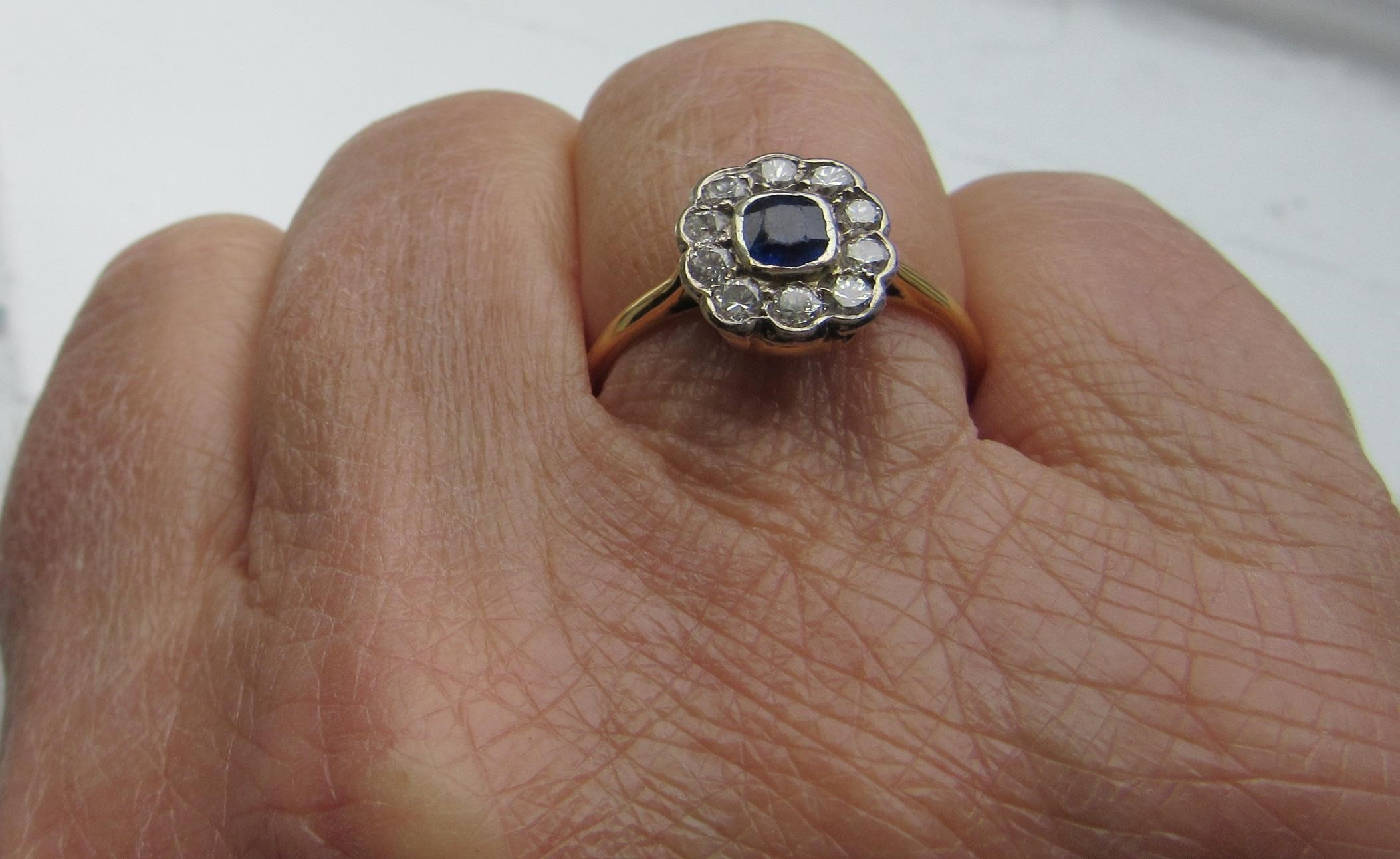 A SAPPHIRE AND DIAMOND CLUSTER RING, the cushion cut sapphire in rub over setting to a border of ten Image