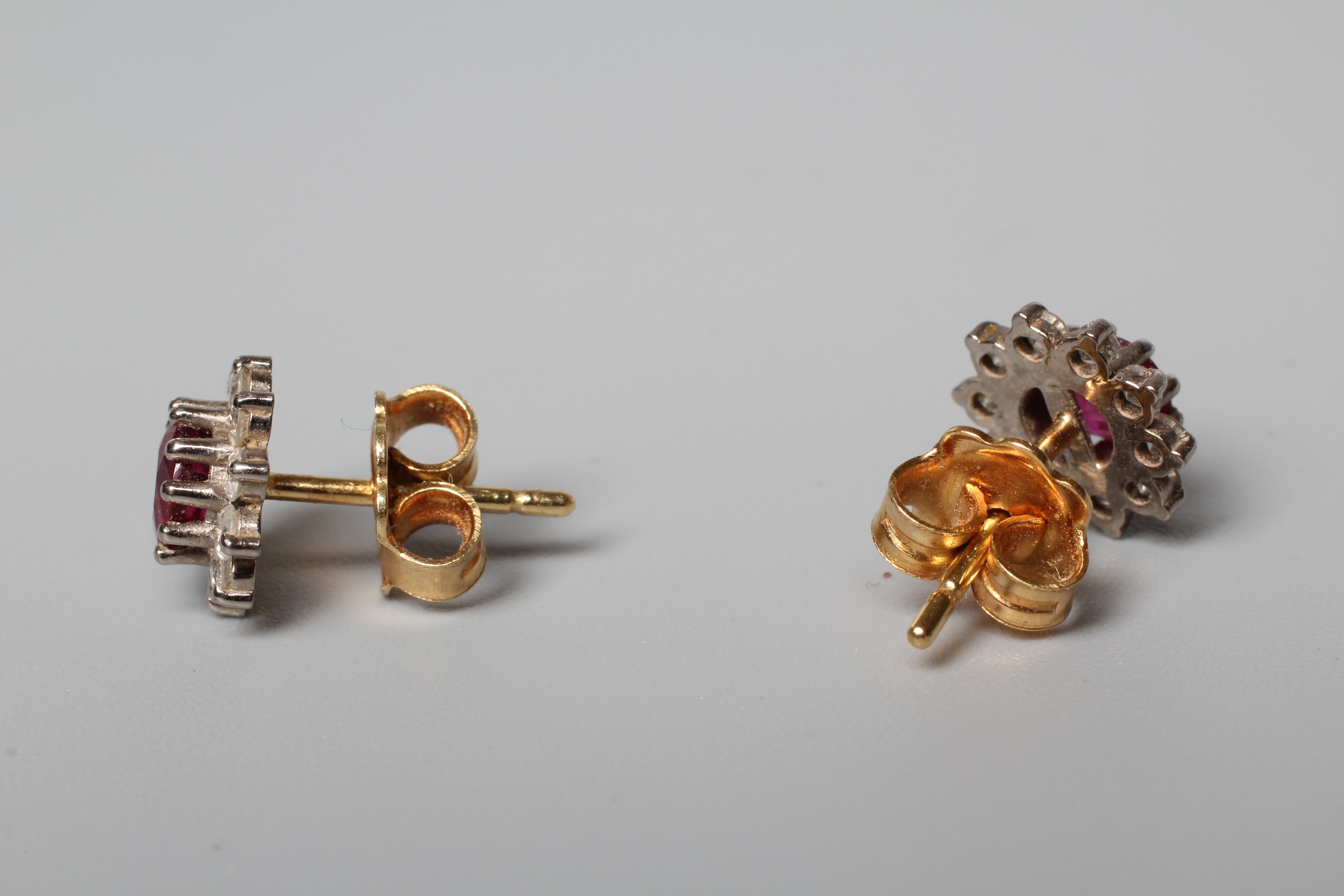 A PAIR OF RUBY AND DIAMOND CLUSTER EAR STUDS, the facet cut circular rubies claw set to borders of Image