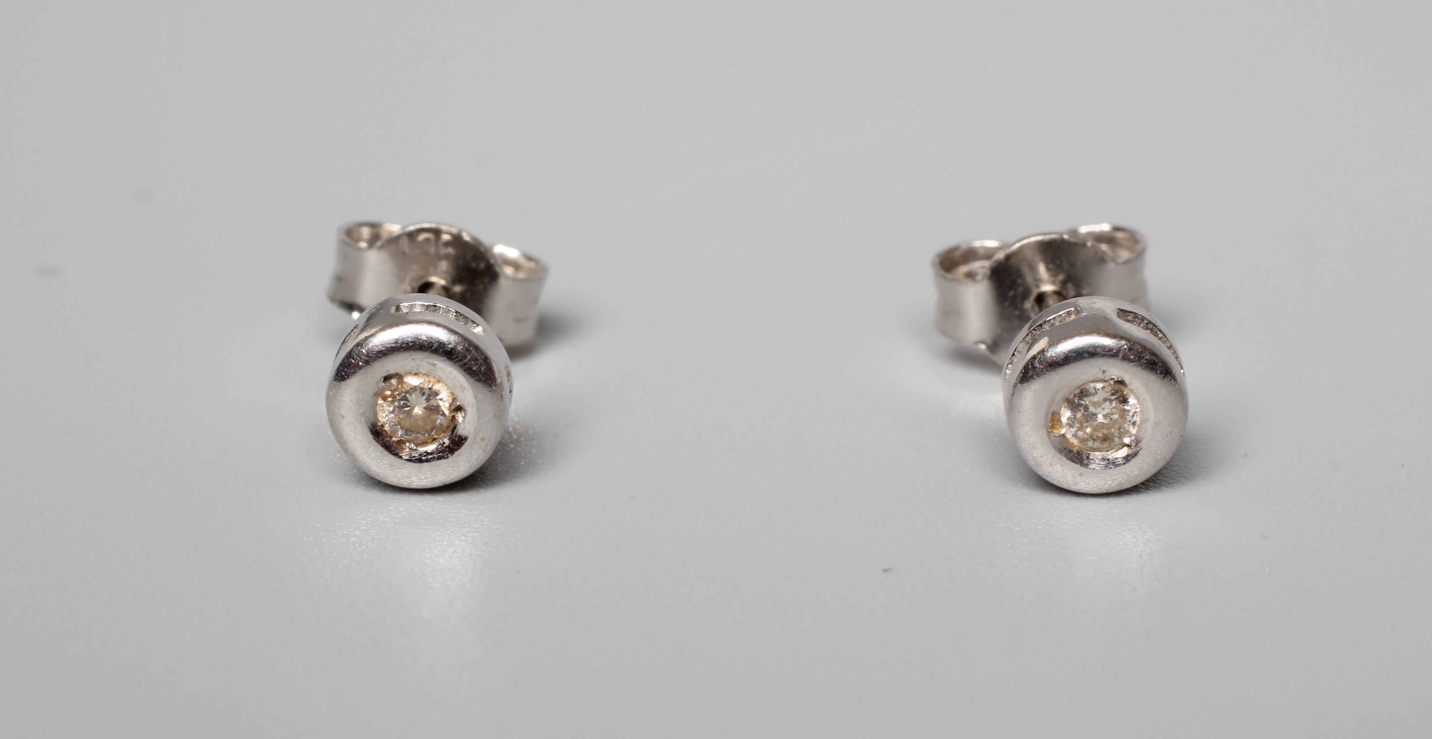 A PAIR OF DIAMOND SOLITAIRE EAR STUDS, the small round brilliant cut stones in rub over settings to Image
