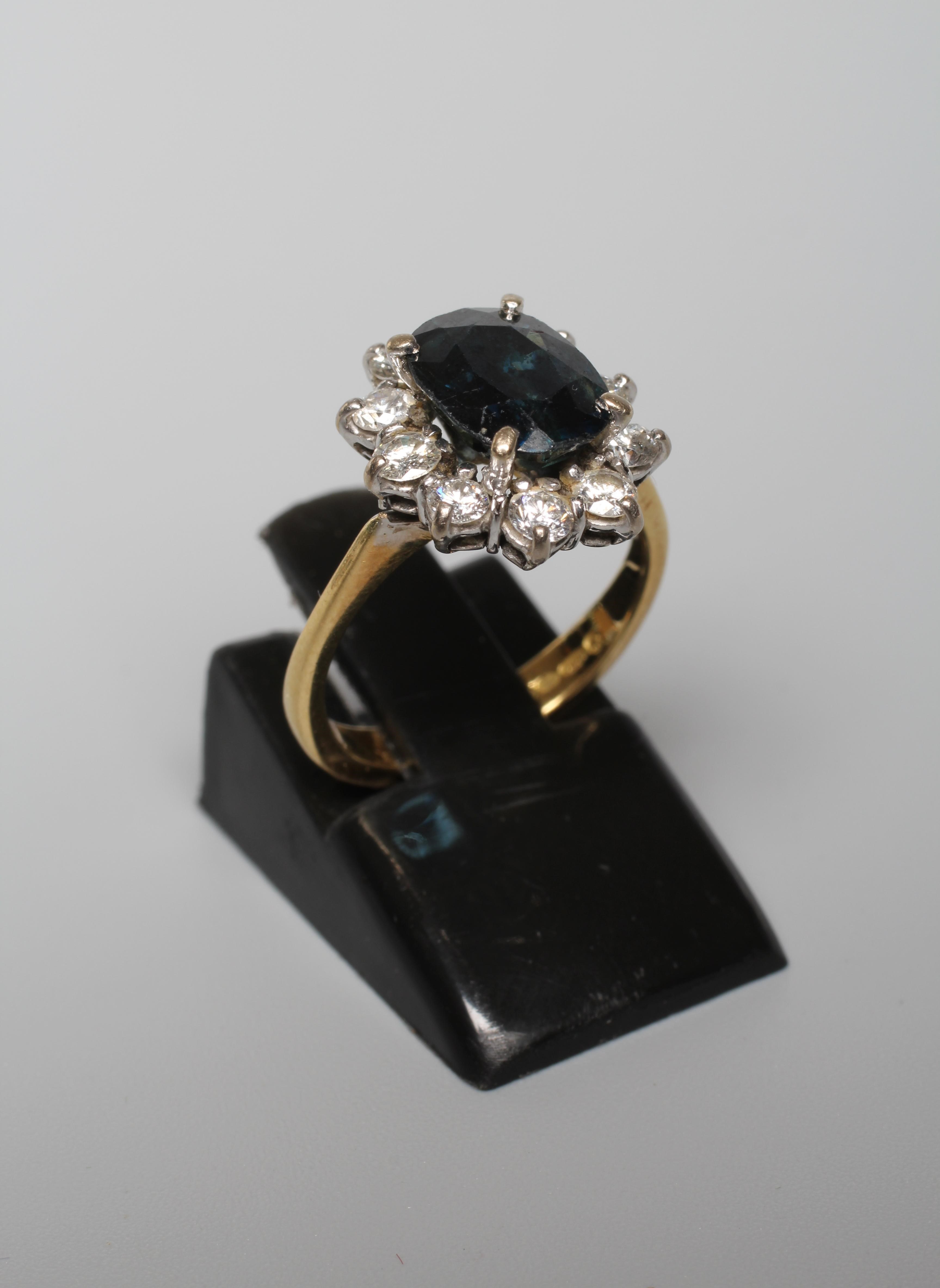 A SAPPHIRE AND DIAMOND CLUSTER RING, the oval facet cut sapphire claw set to a border of ten round Image