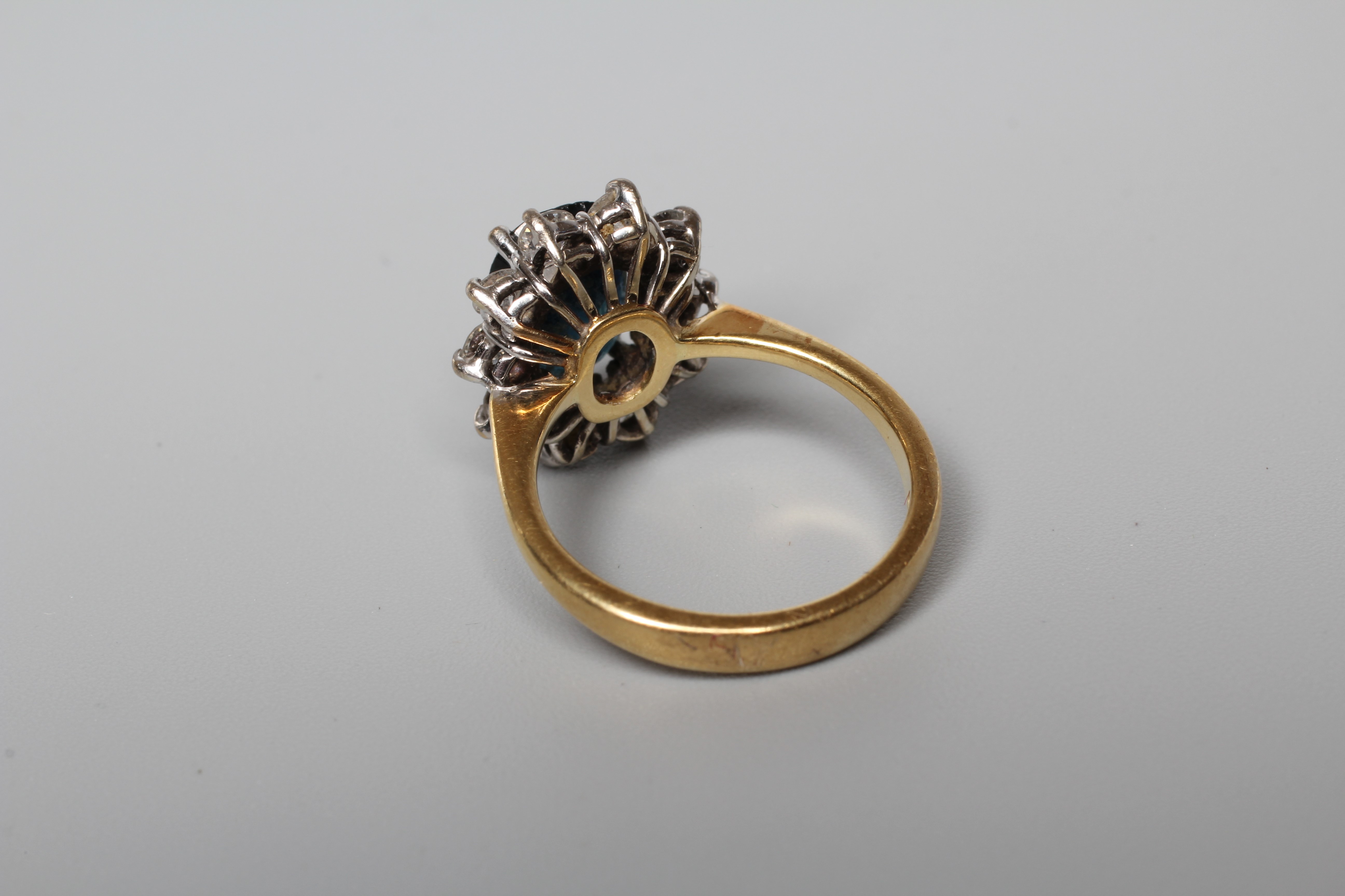 A SAPPHIRE AND DIAMOND CLUSTER RING, the oval facet cut sapphire claw set to a border of ten round Image