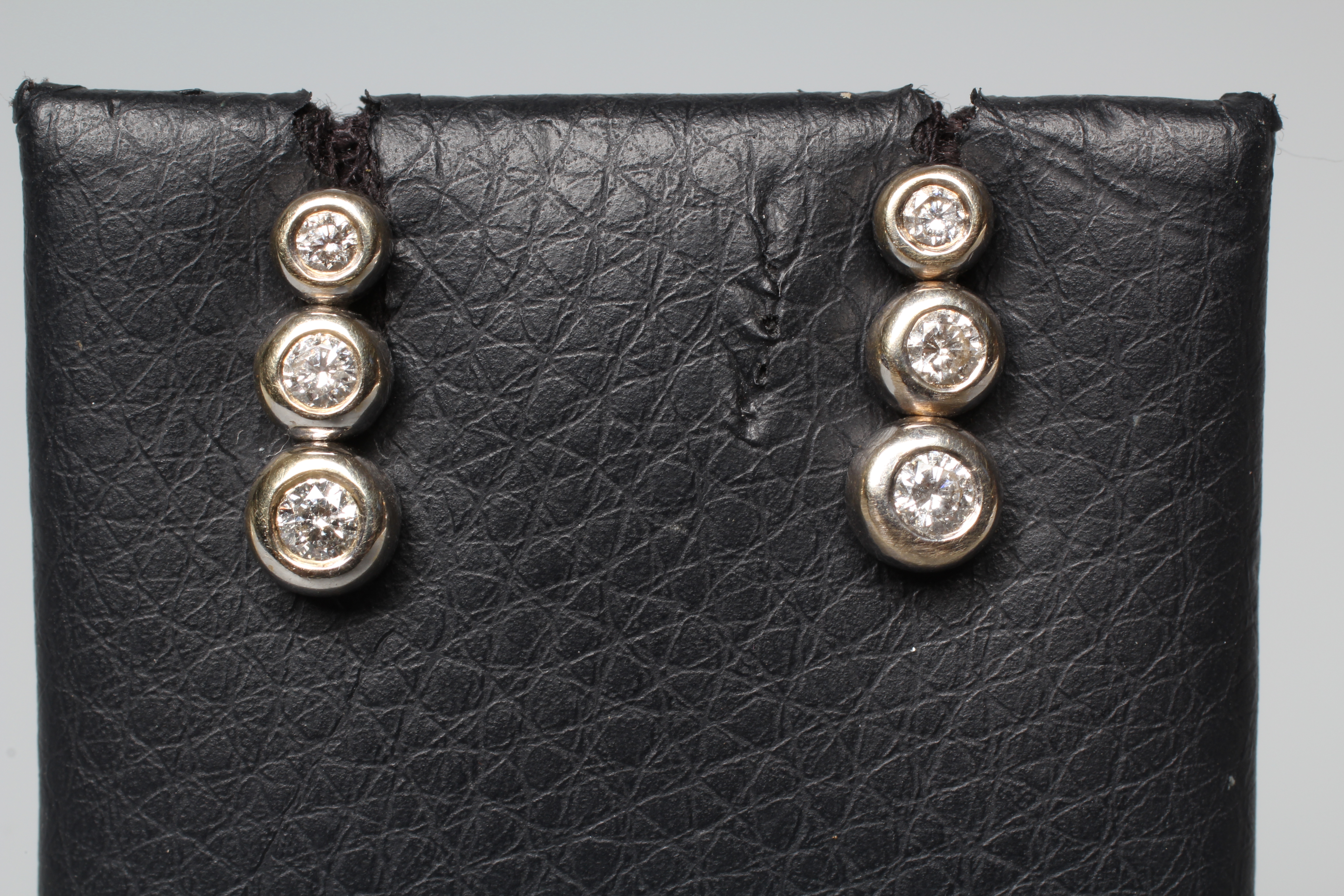 A PAIR OF DIAMOND EAR STUDS, the three graduating round brilliants in rub over settings to Image