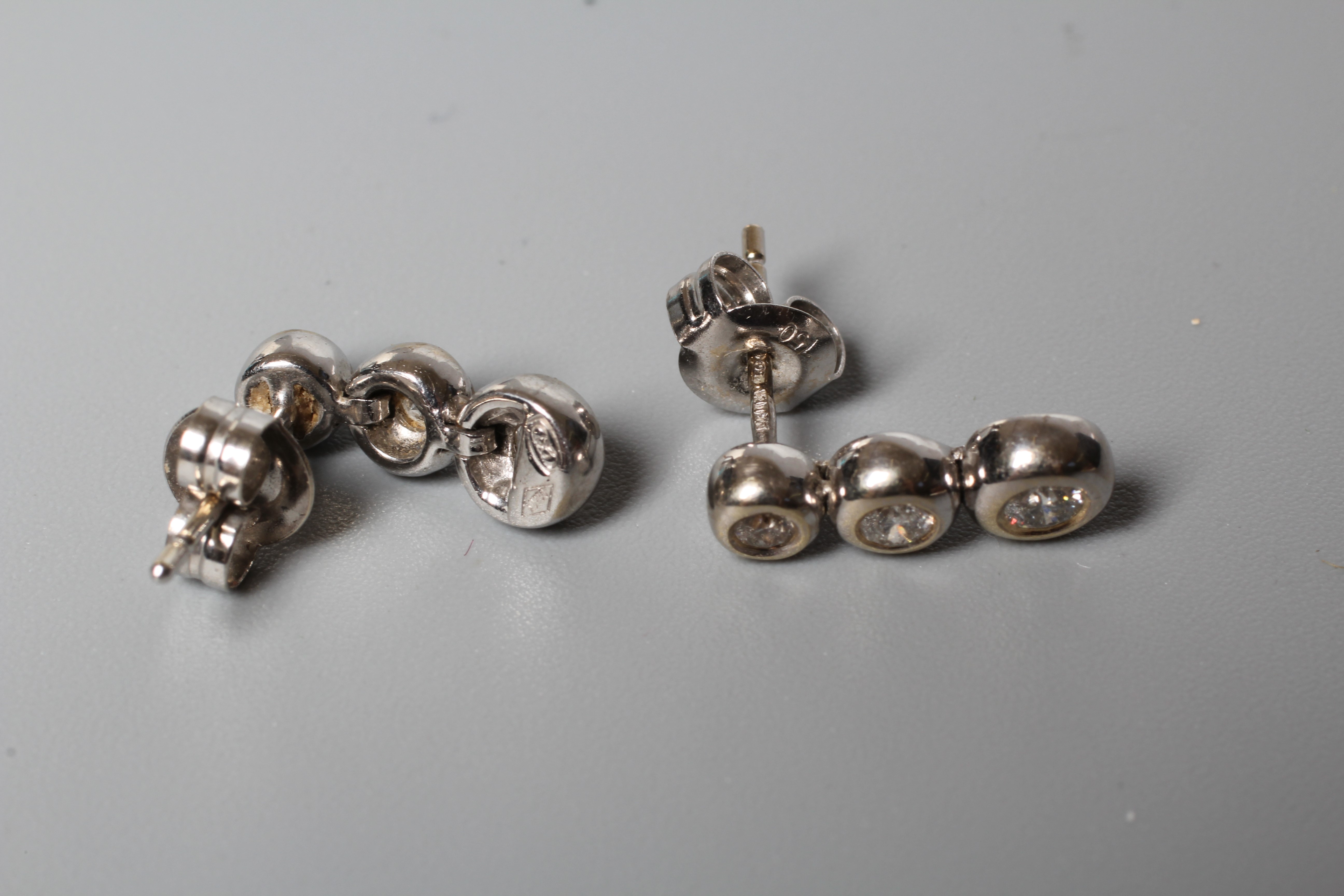 A PAIR OF DIAMOND EAR STUDS, the three graduating round brilliants in rub over settings to Image