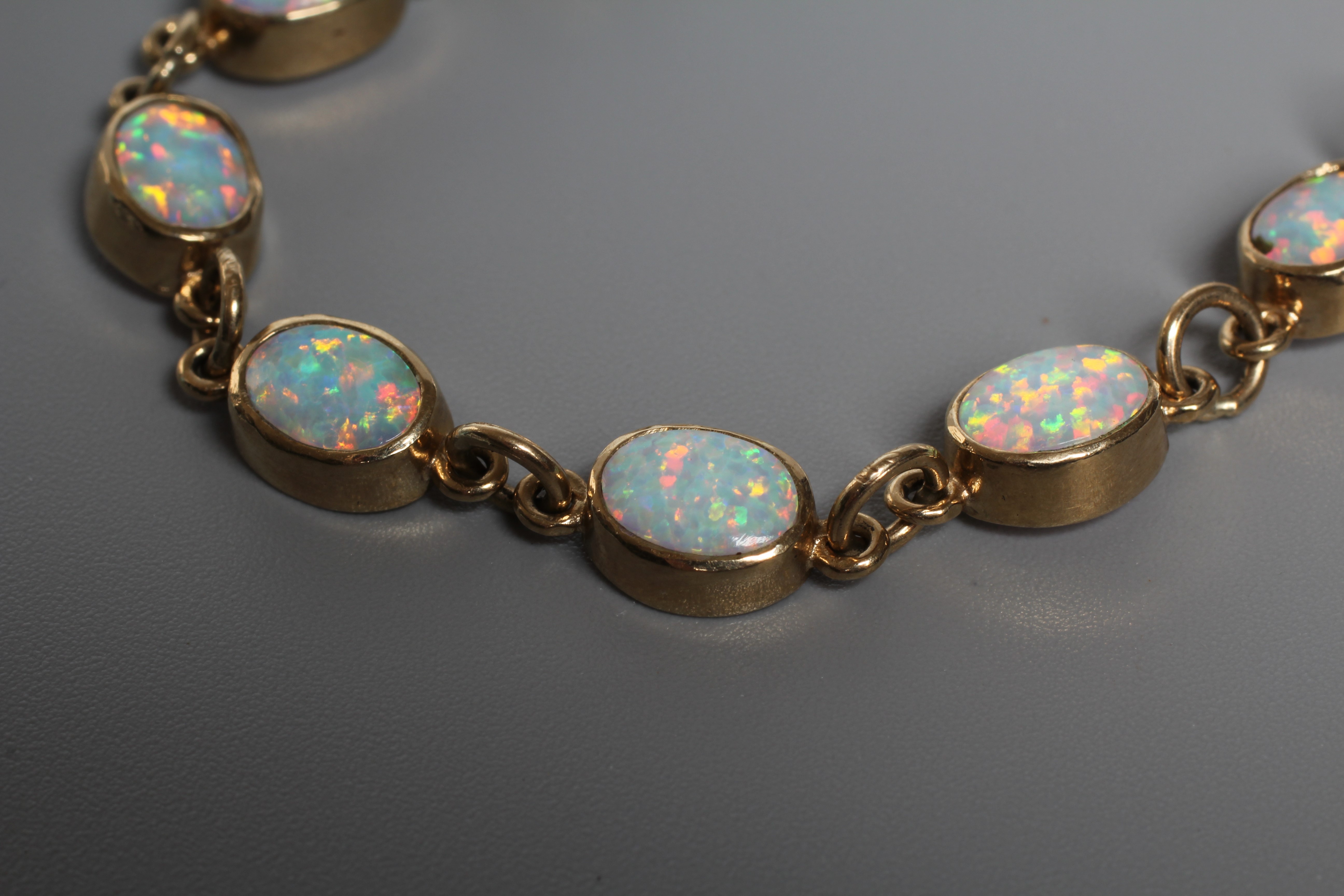 AN OPAL BRACELET, the fourteen oval cabochon polished stones open back collet set to a plain frame Image