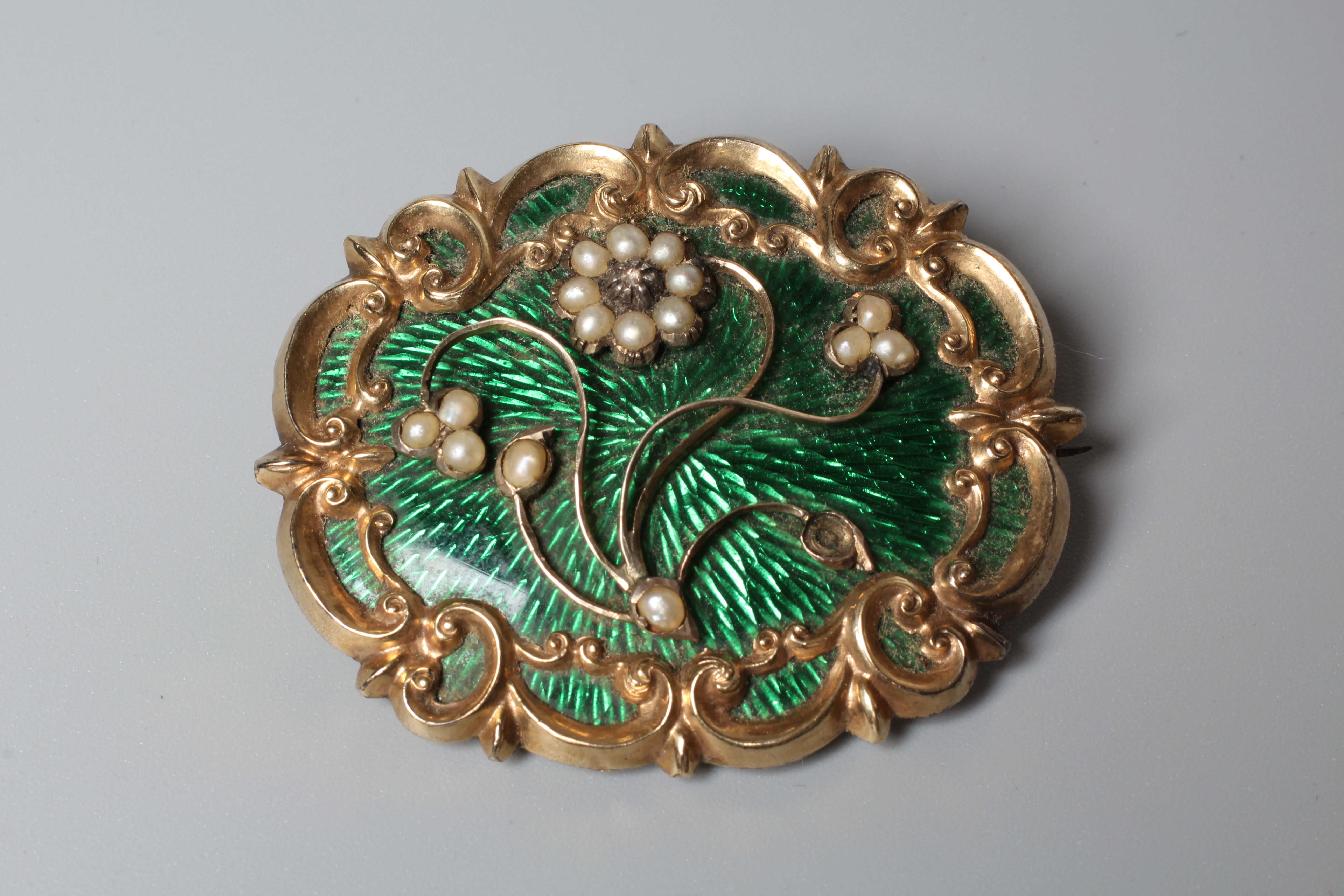 A VICTORIAN OVAL BROOCH, the green guilloche enamel ground overlaid with a scrolling border Image