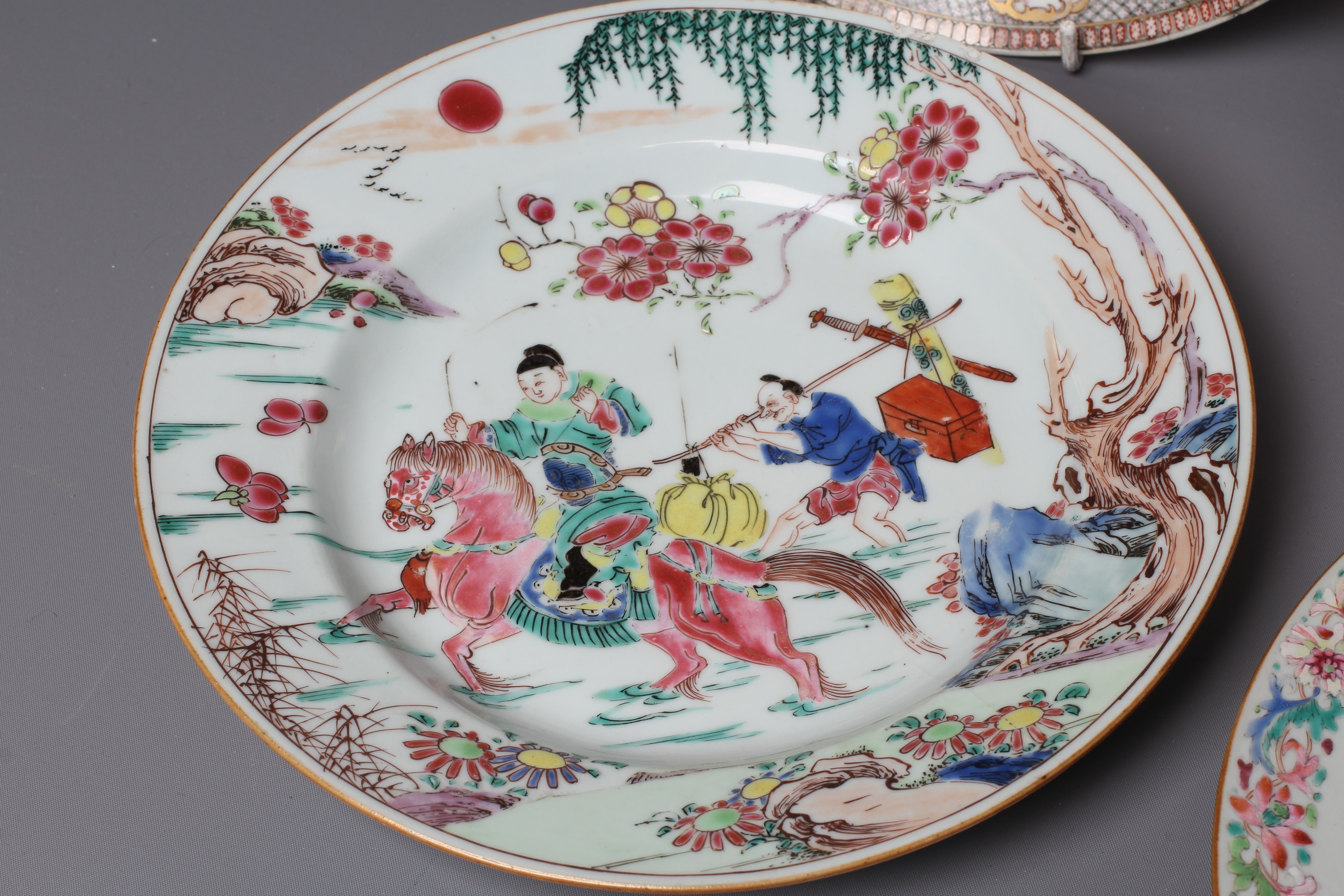 FOUR CHINESE FAMILLE ROSE PORCELAIN PLATES comprising a saucer dish with figures and dogs on a Image