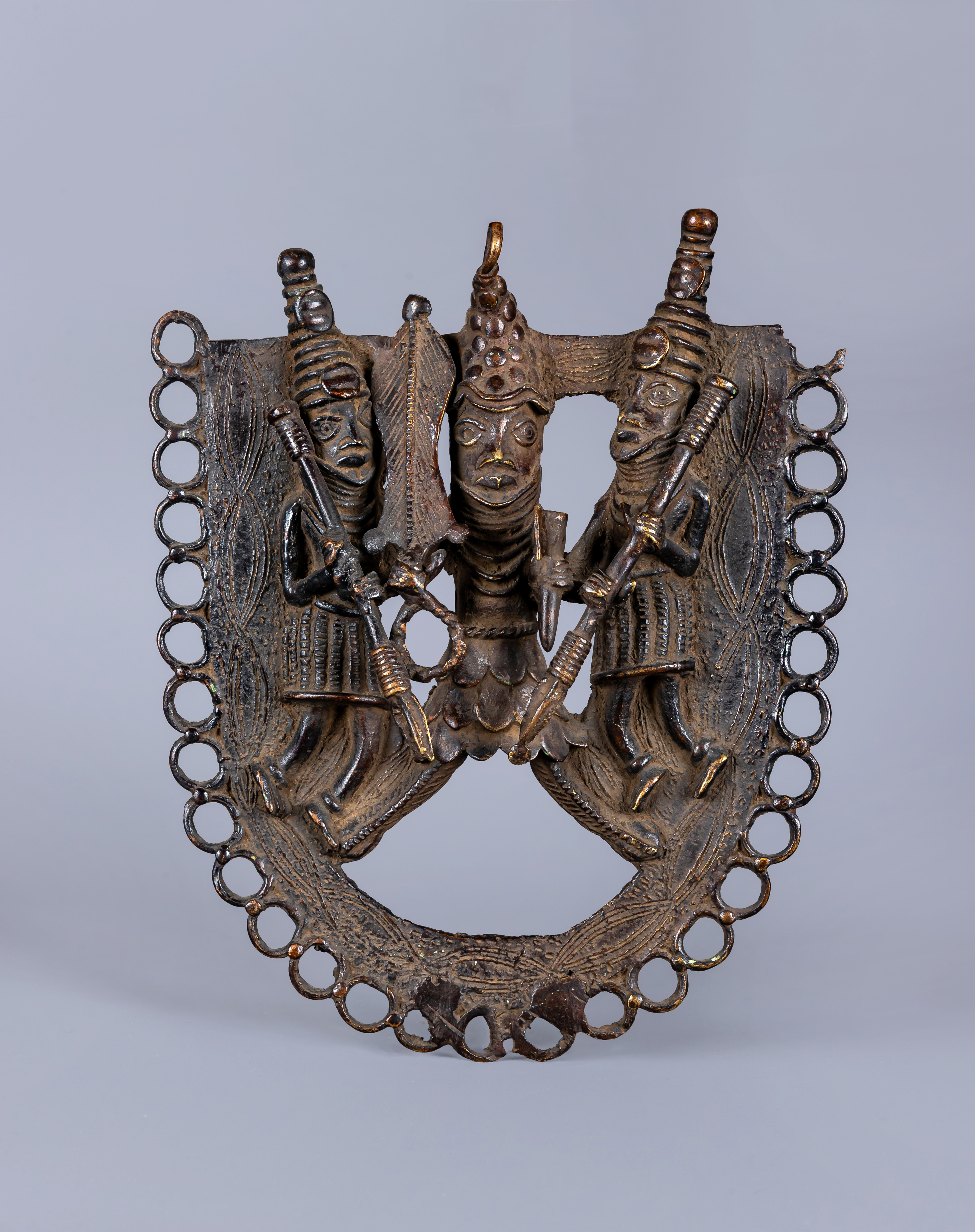 A BENIN PATINATED BRONZE PLAQUE worked in relief with three warriors within a stylised ringlet Image