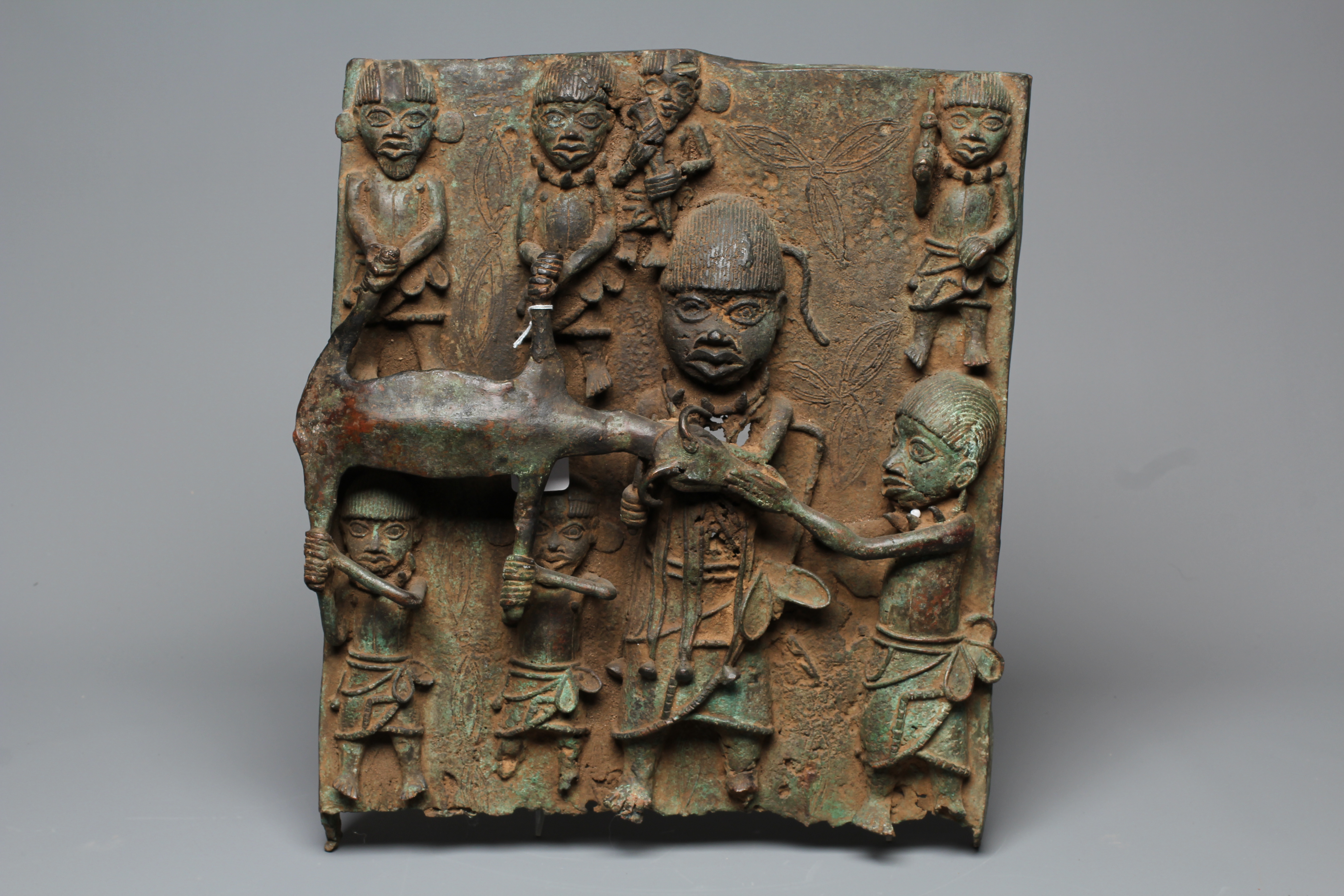 A BENIN BRONZE PLAQUE worked in relief depicting Obas butchers carrying a sacrificial cow, 18 1/2" Image