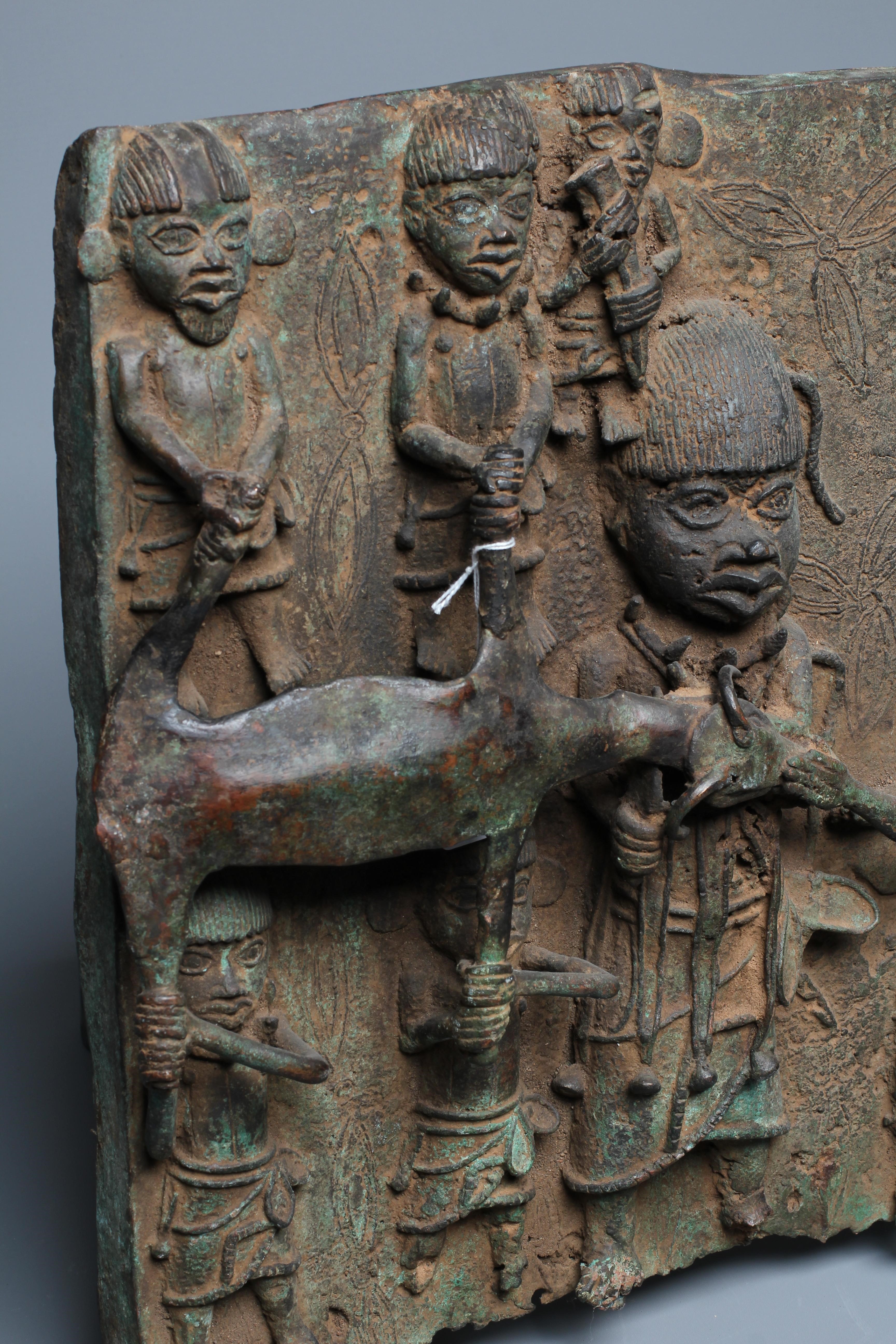 A BENIN BRONZE PLAQUE worked in relief depicting Obas butchers carrying a sacrificial cow, 18 1/2" Image