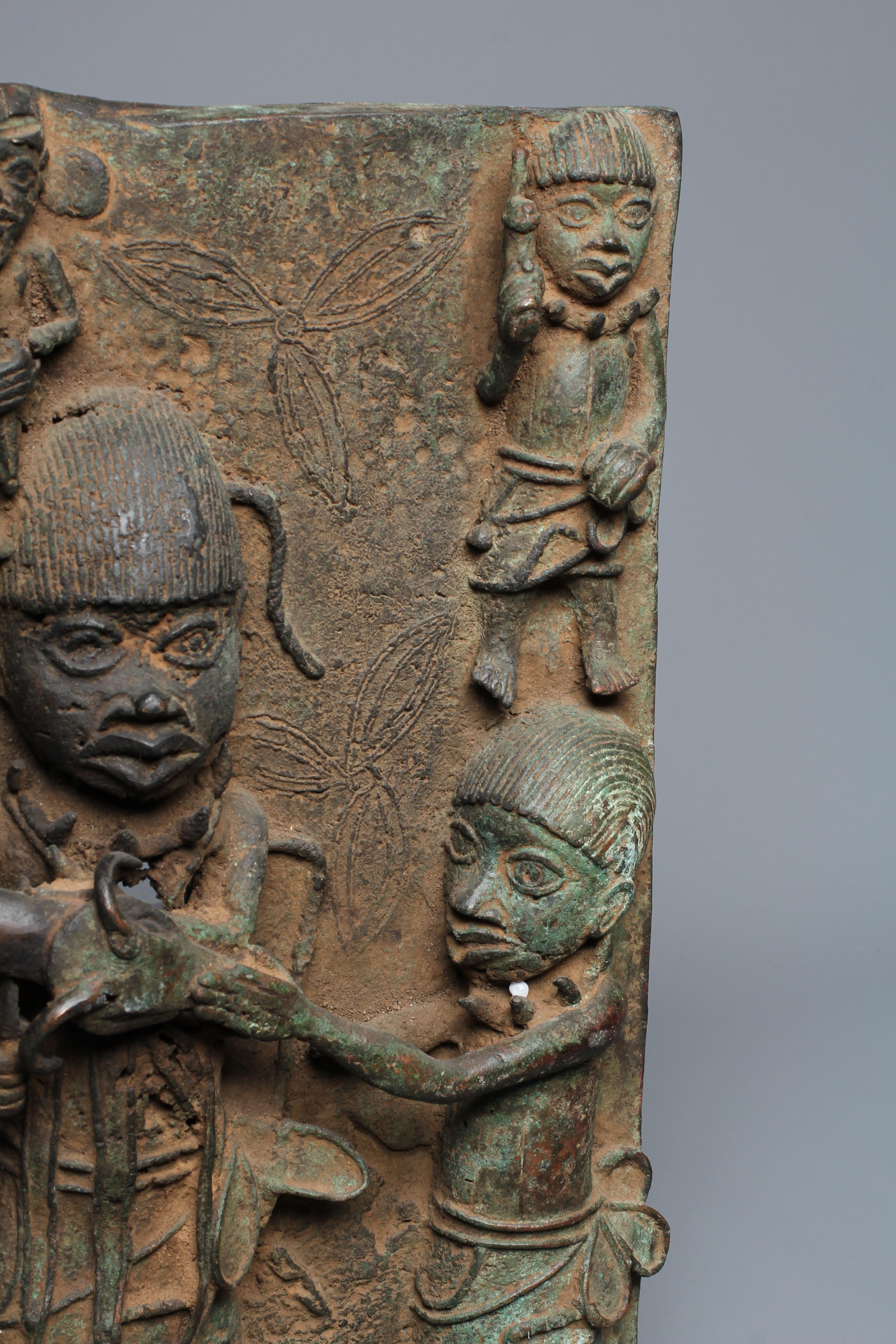 A BENIN BRONZE PLAQUE worked in relief depicting Obas butchers carrying a sacrificial cow, 18 1/2" Image