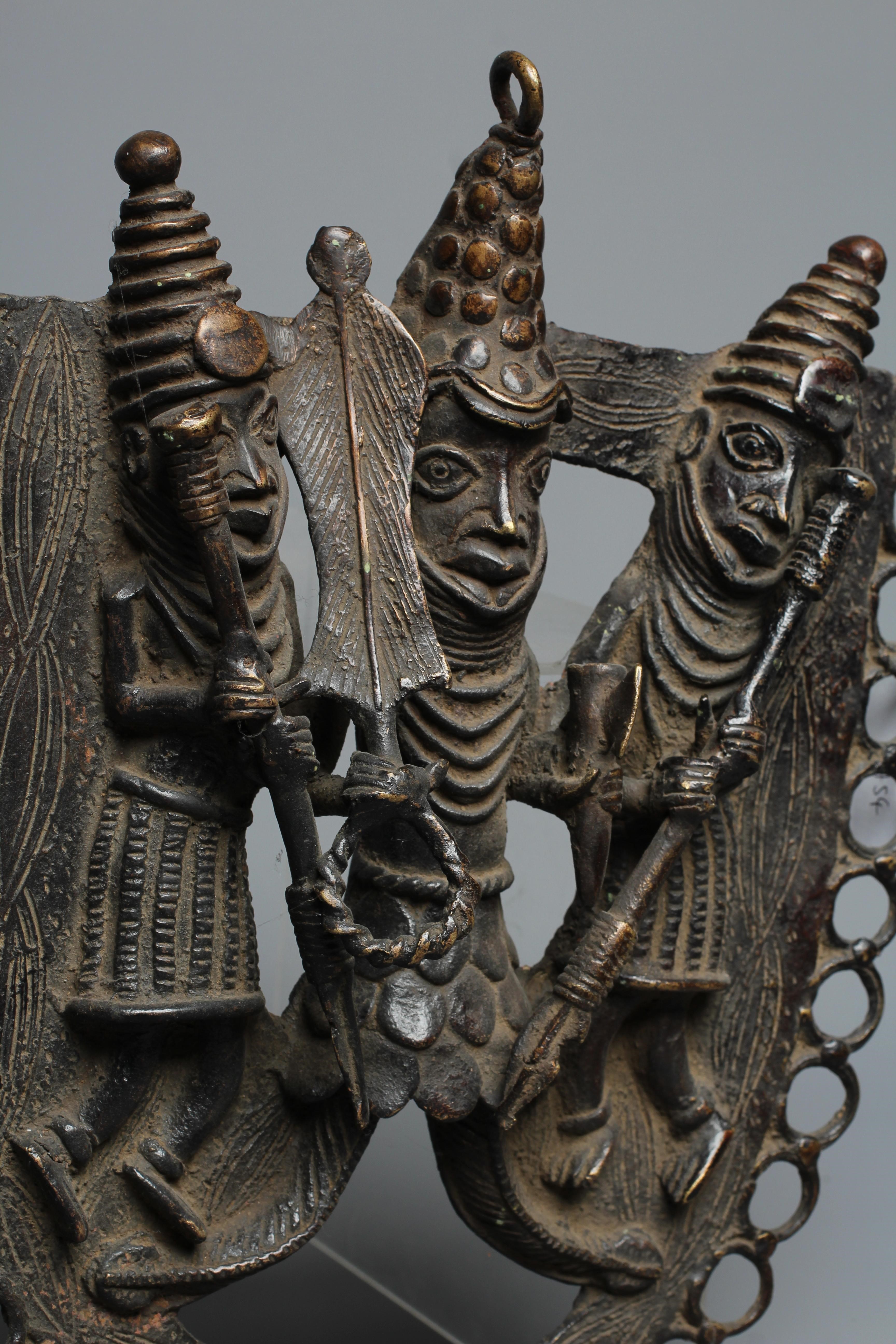 A BENIN PATINATED BRONZE PLAQUE worked in relief with three warrior figures within a stylised Image