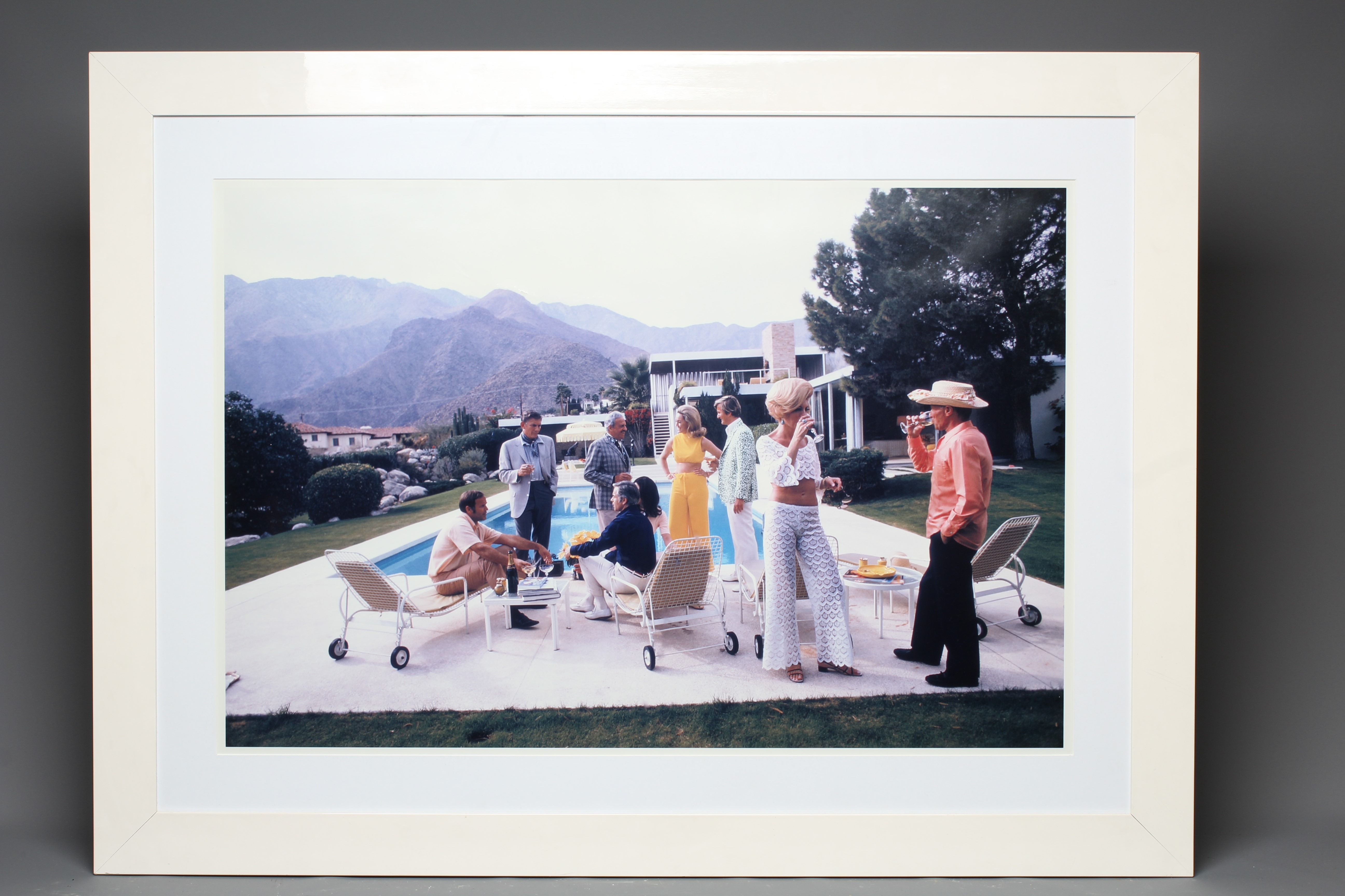 AFTER SLIM AARONS (1916-2000) Desert House Party, photographic print, 26" x 39" (SH), framed and Image