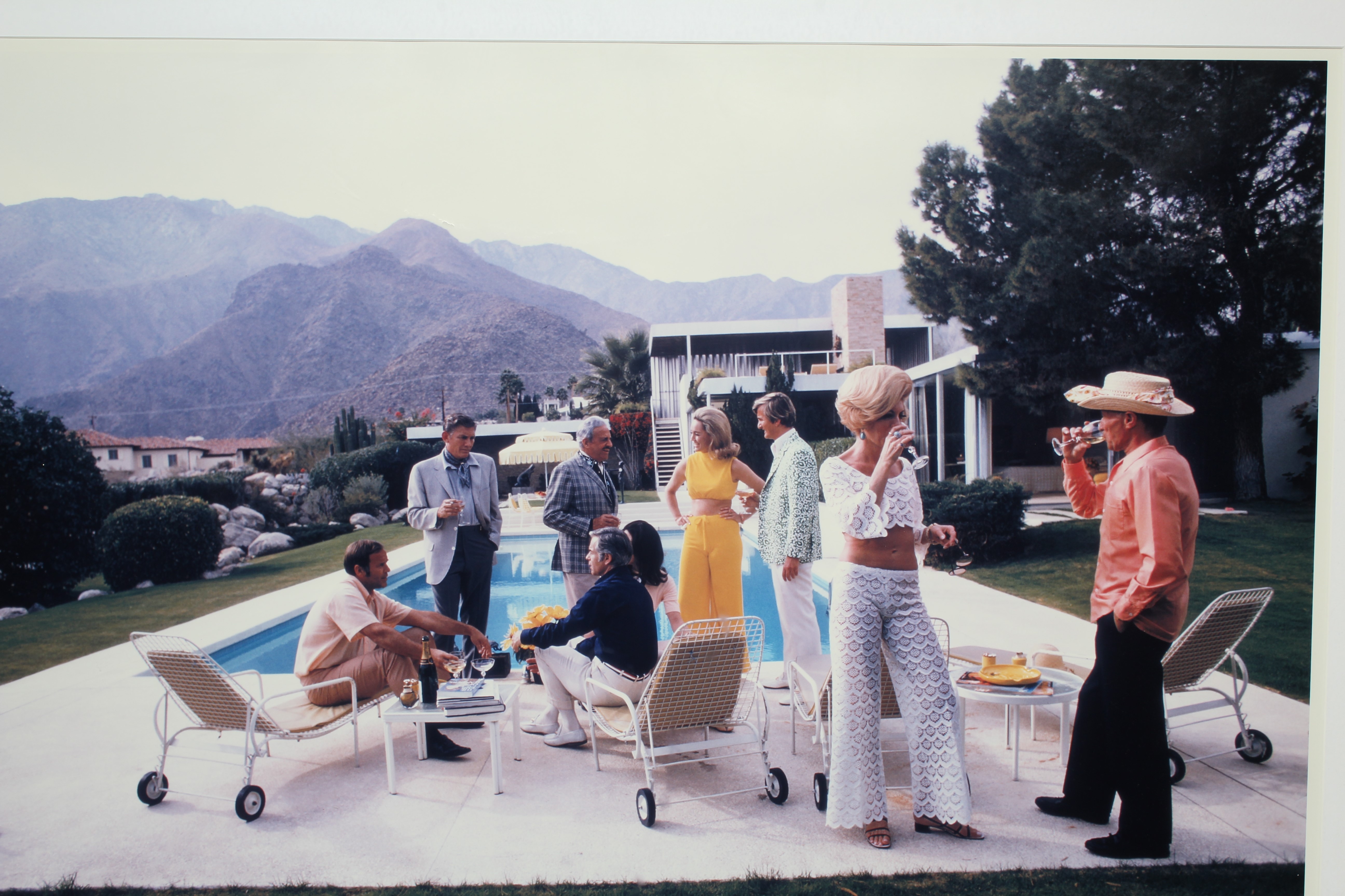 AFTER SLIM AARONS (1916-2000) Desert House Party, photographic print, 26" x 39" (SH), framed and Image