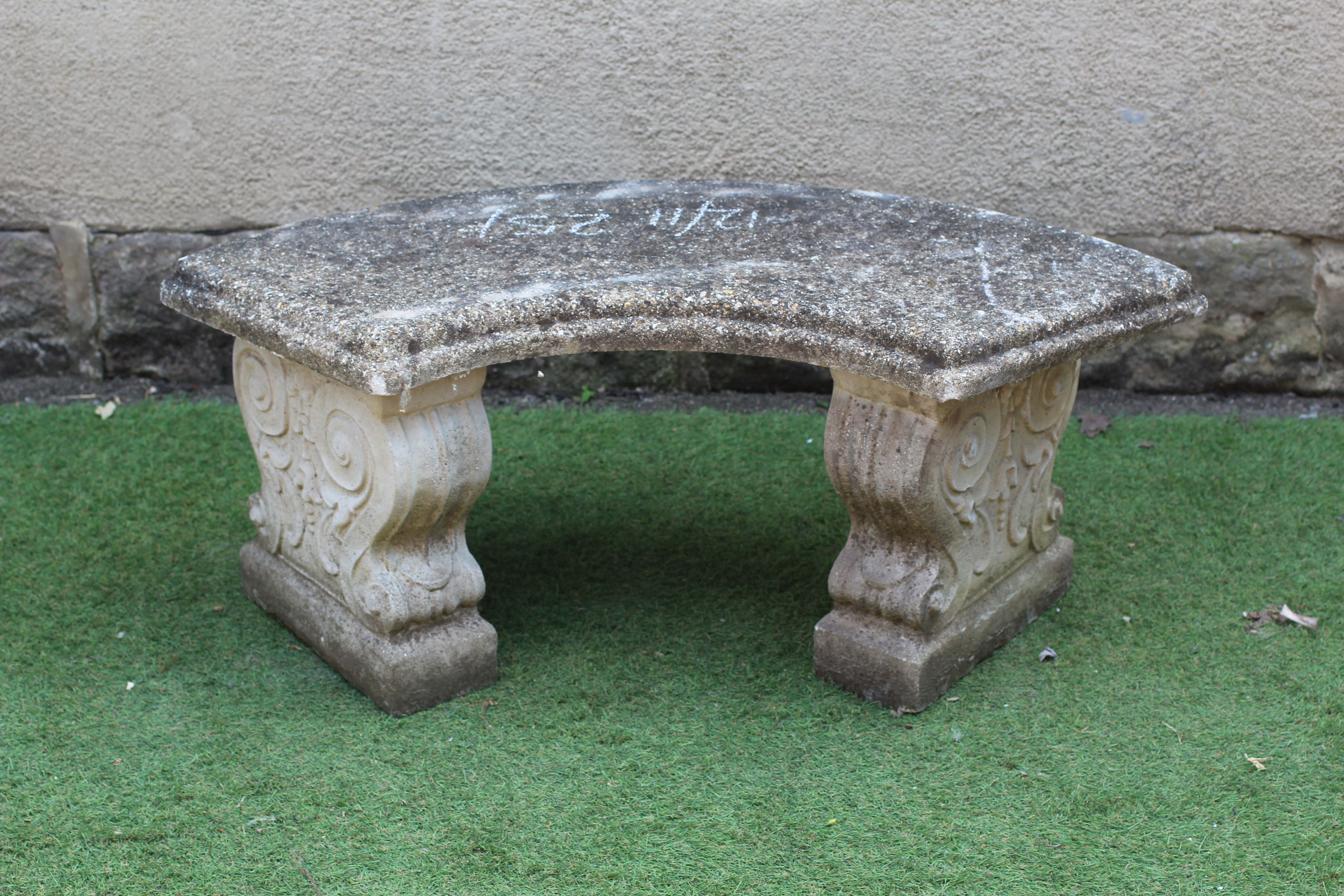 A CAST STONE BENCH, the moulded edged crescent shaped seat raised on waisted scroll moulded end Image