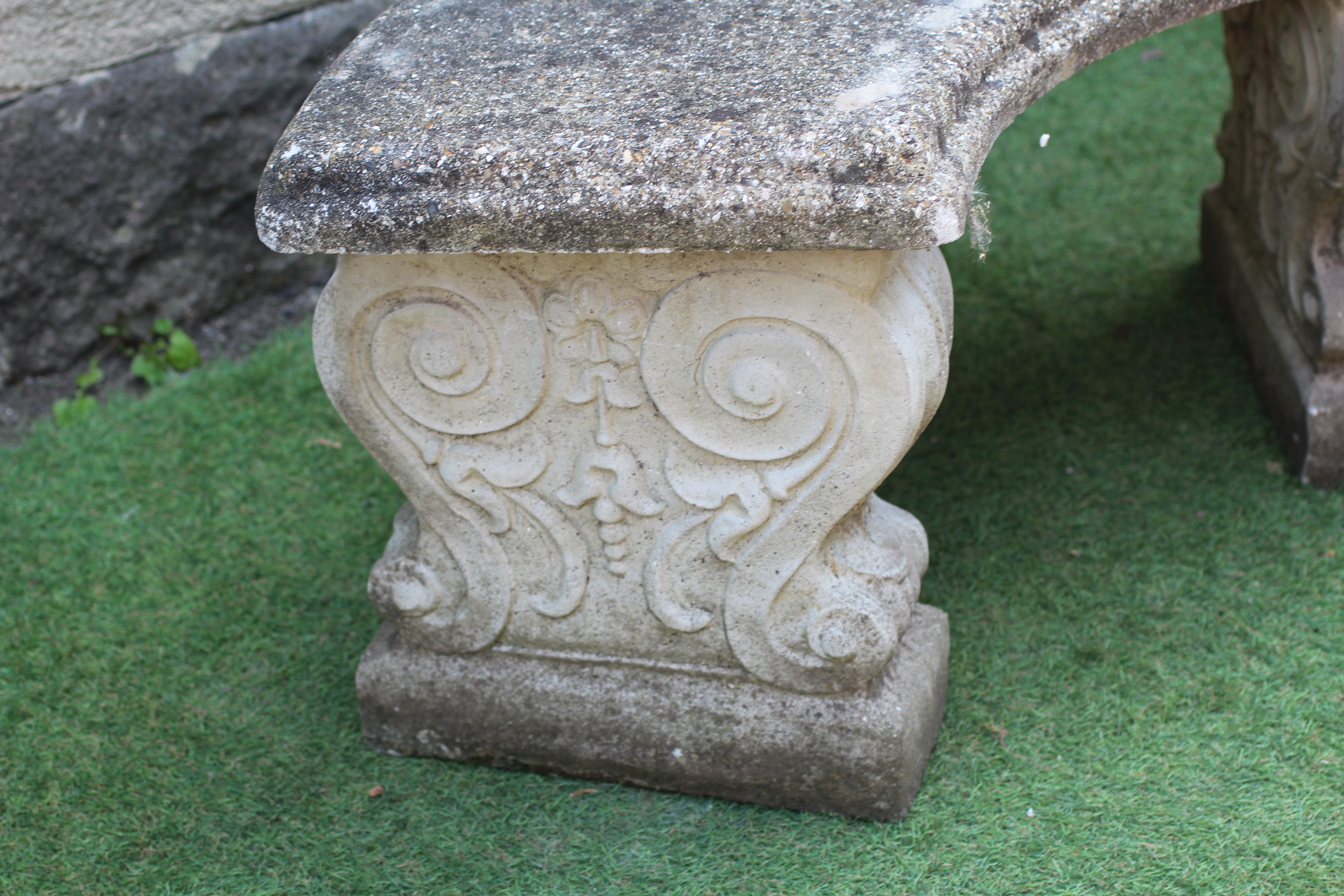 A CAST STONE BENCH, the moulded edged crescent shaped seat raised on waisted scroll moulded end Image