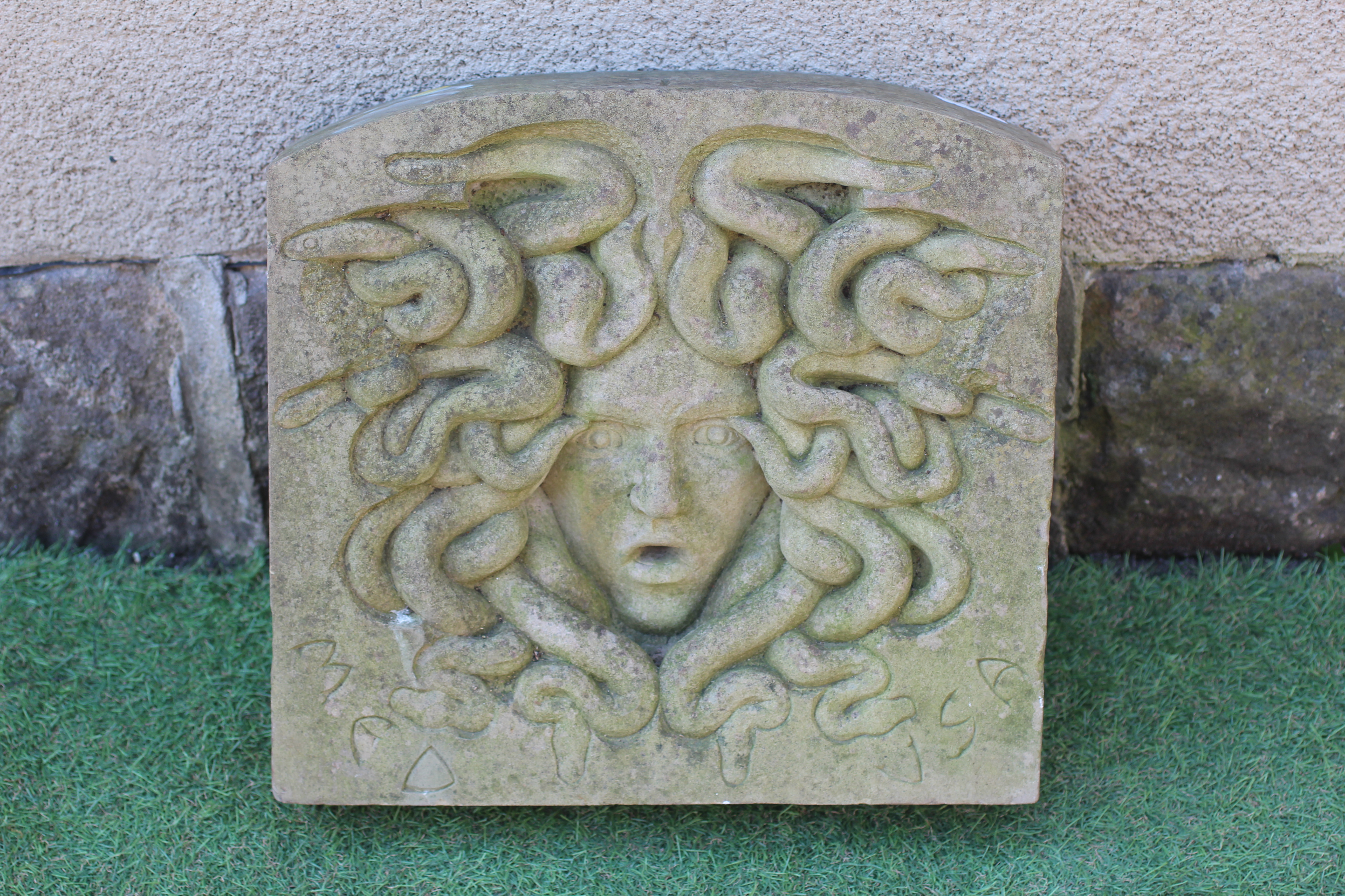 A CARVED SANDSTONE WALL PLAQUE of arched oblong form and depicting the head of Medusa, inscribed Image