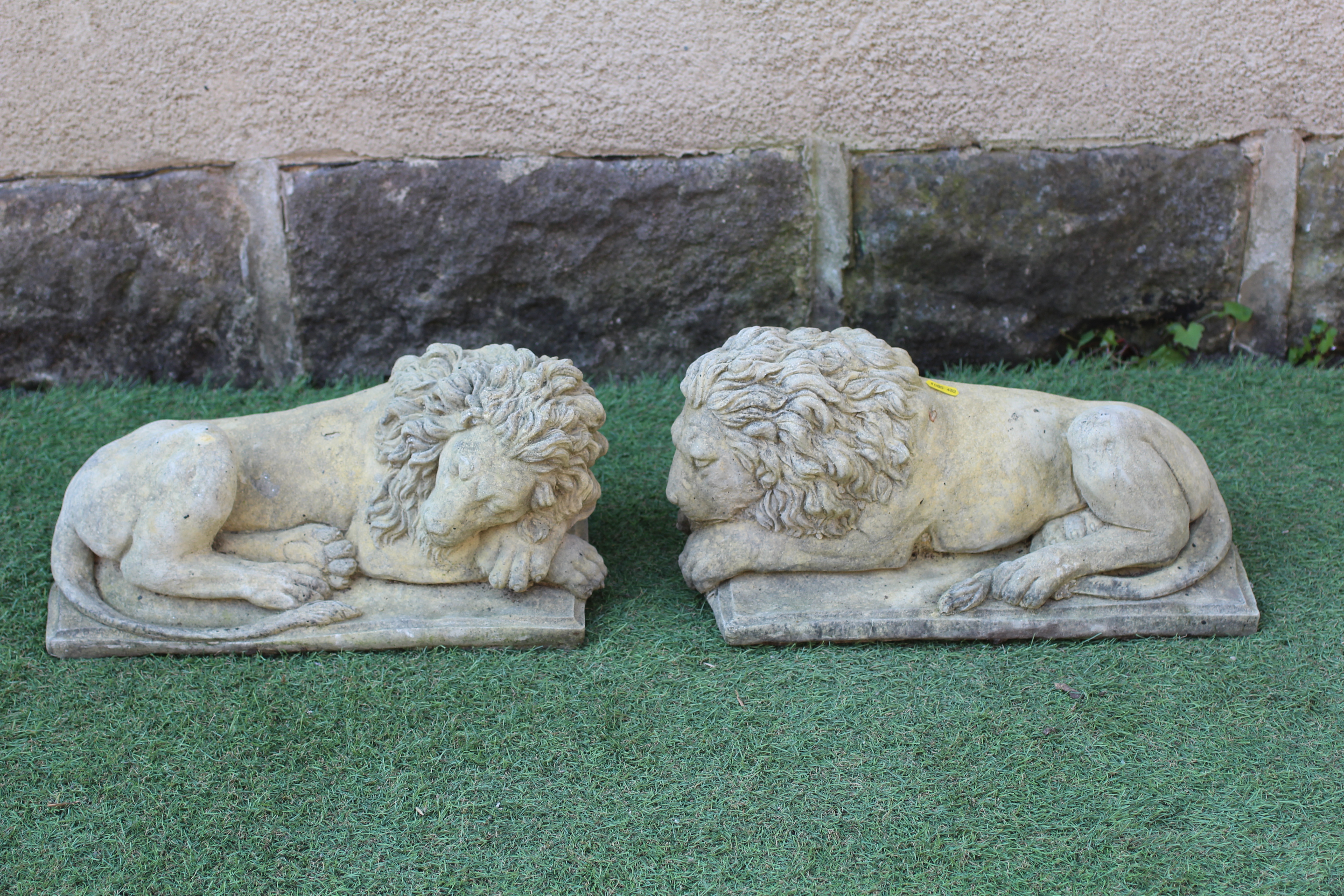 A PAIR OF CAST STONE RECUMBENT LIONS on square bases, 17" w x 8" d x 8 1/2" h Image