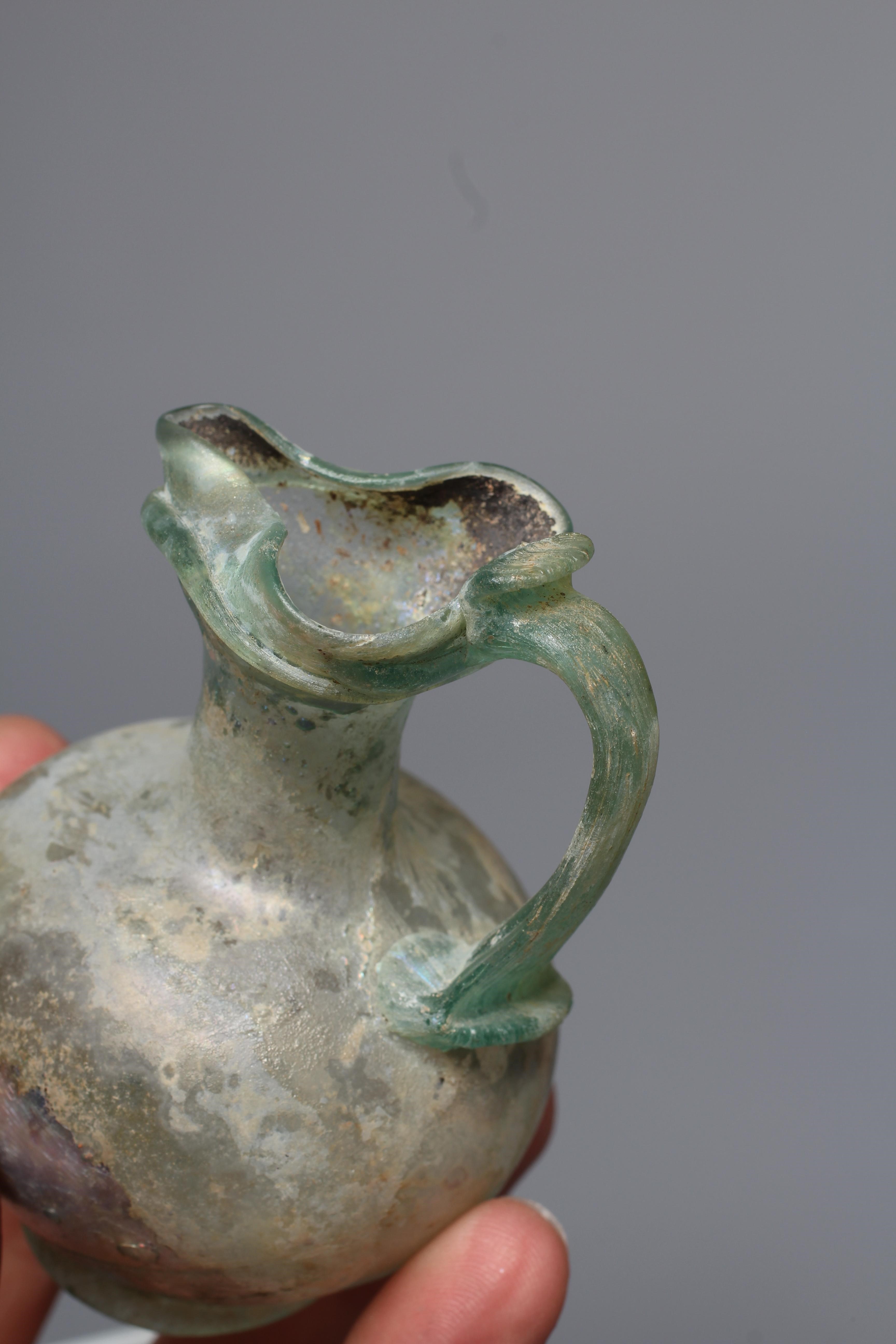 A ROMAN GREEN GLASS JUG, 3rd-4th century AD, with trefoil lip and pulled handle, 3 1/2" high, Image