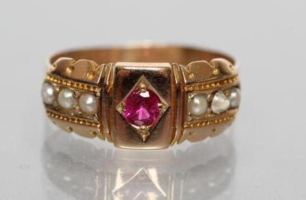 A LATE VICTORIAN 15CT GOLD RING centred by a gypsy set ruby within panelled shoulders each set with Image